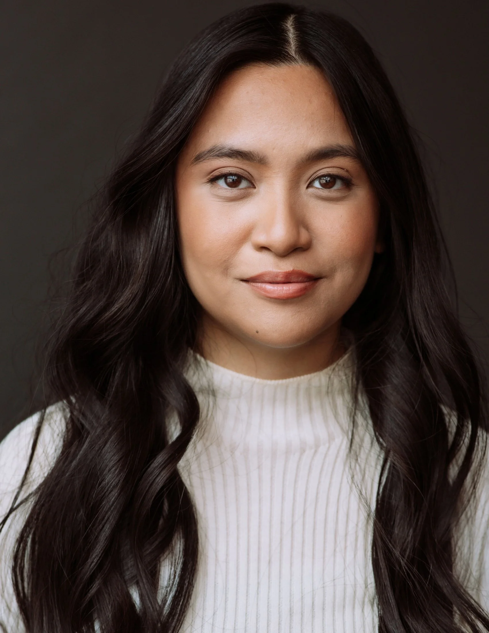 Jona, a Filipino-Canadian woman, is smiling softly at the camera. She has long brown hair and is wearing a white mock neck top.