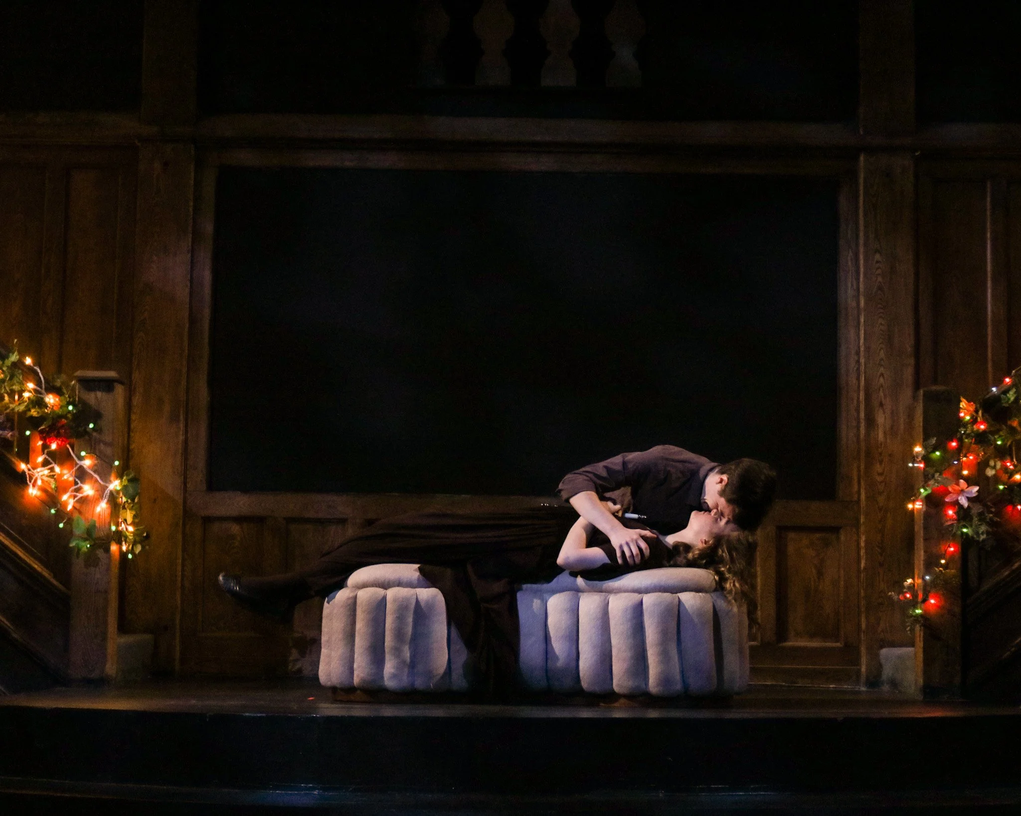 From Romeo and Juliet 2023. Romeo is resting his forehead against Juliet's, she is laying on a pedestal as though entombed. There are fairy lights on either side of the stage, on railings.