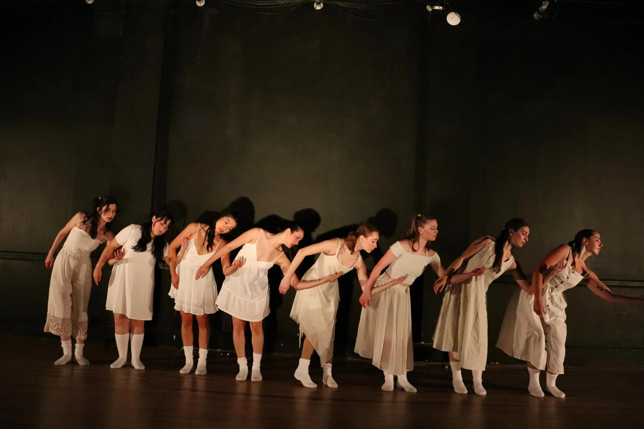 a group of women dressed in a range of all-white outfits are dancing in front of a black background