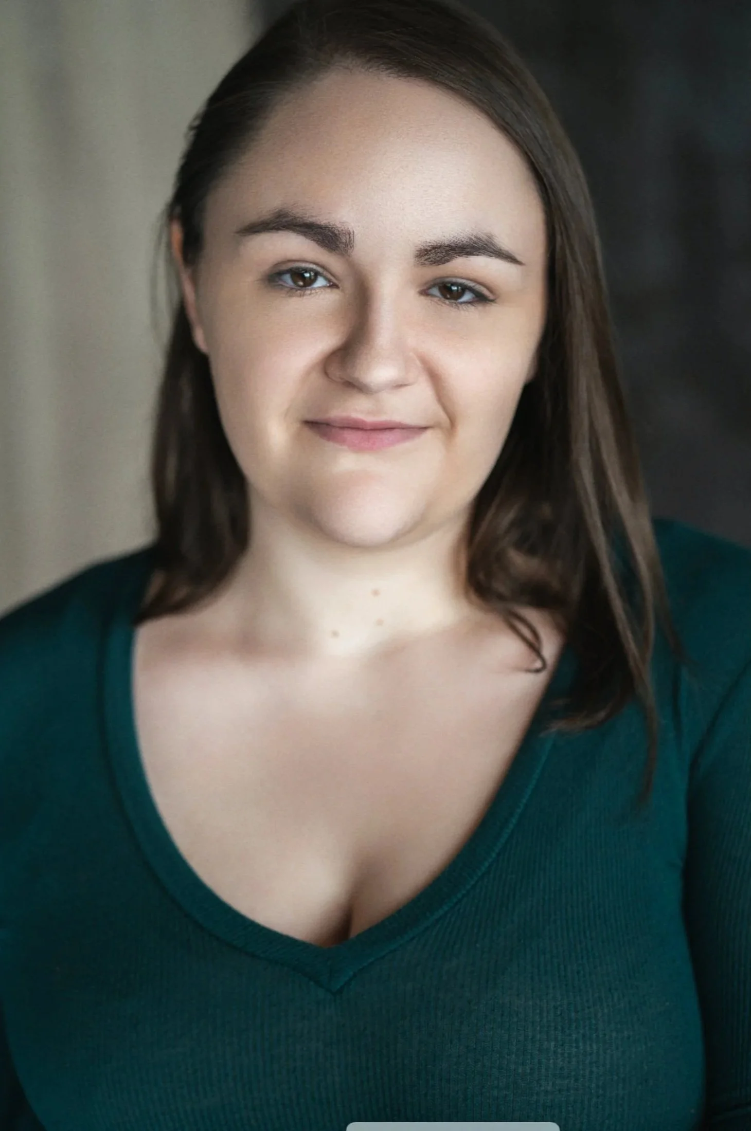 Clair is an indigenous nonbinary performer, with long brown hair, and kind brown eyes. They are looking to camera, wearing a teal sweater, with a grey background.