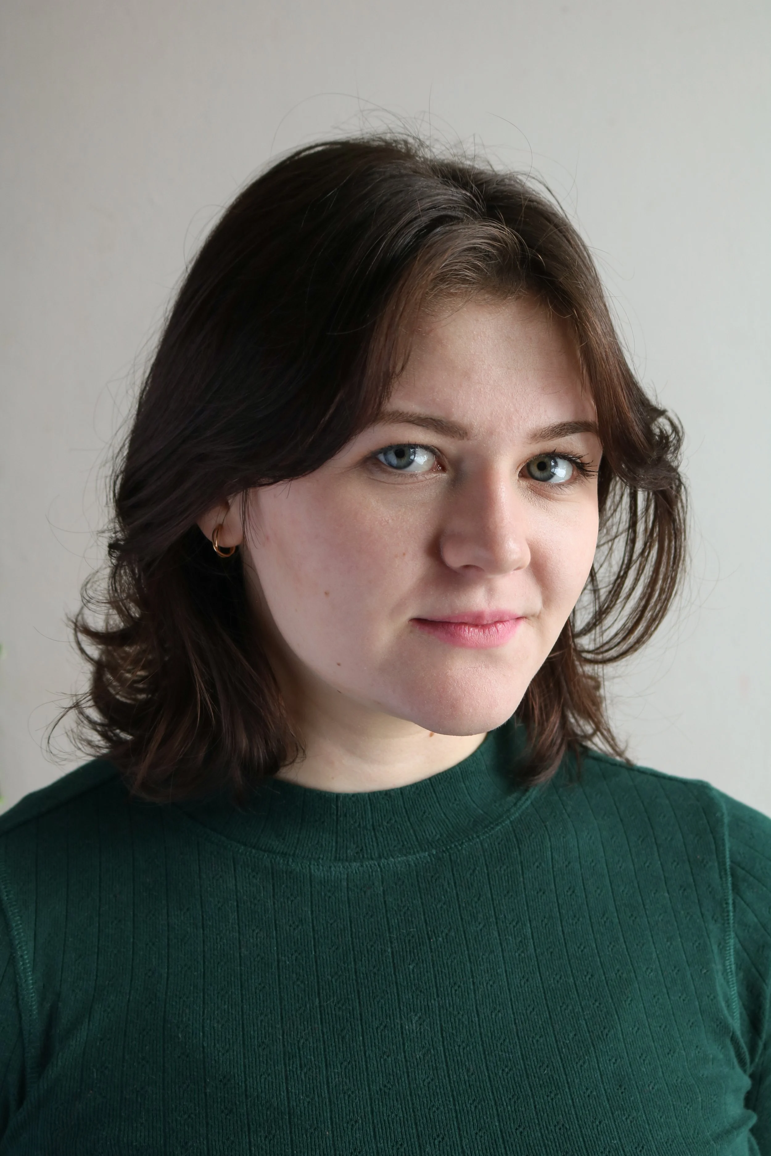 Cheyenne, a white woman, is smiling softly at the camera. She has short brown hair, and is wearing a green sweater that matches her eyes. The background is white.