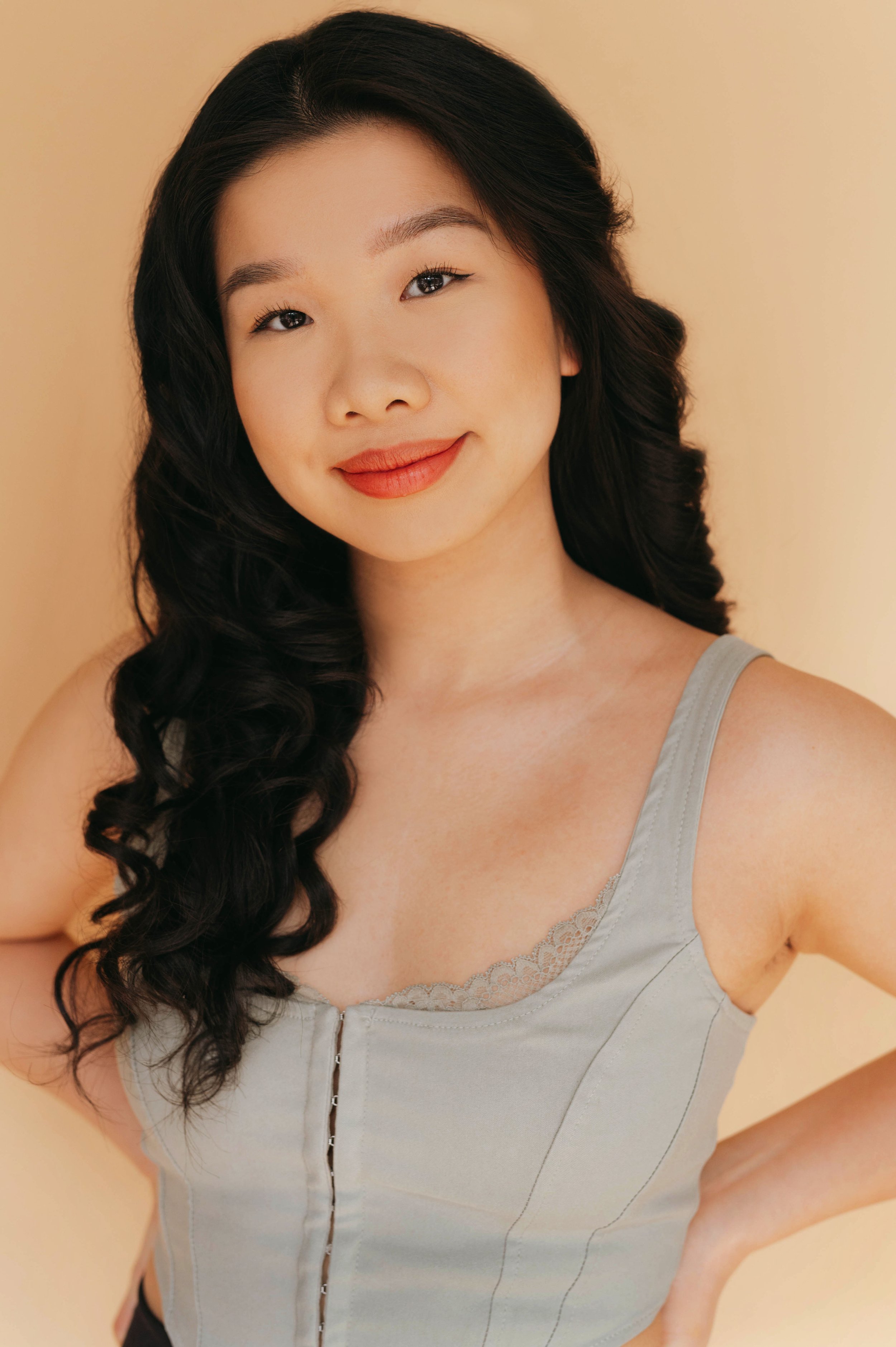 Joanne, a Chinese-Canadian woman, is smiling softly at the camera. She has long black hair, and is wearing a sage green corset top. The background is beige.