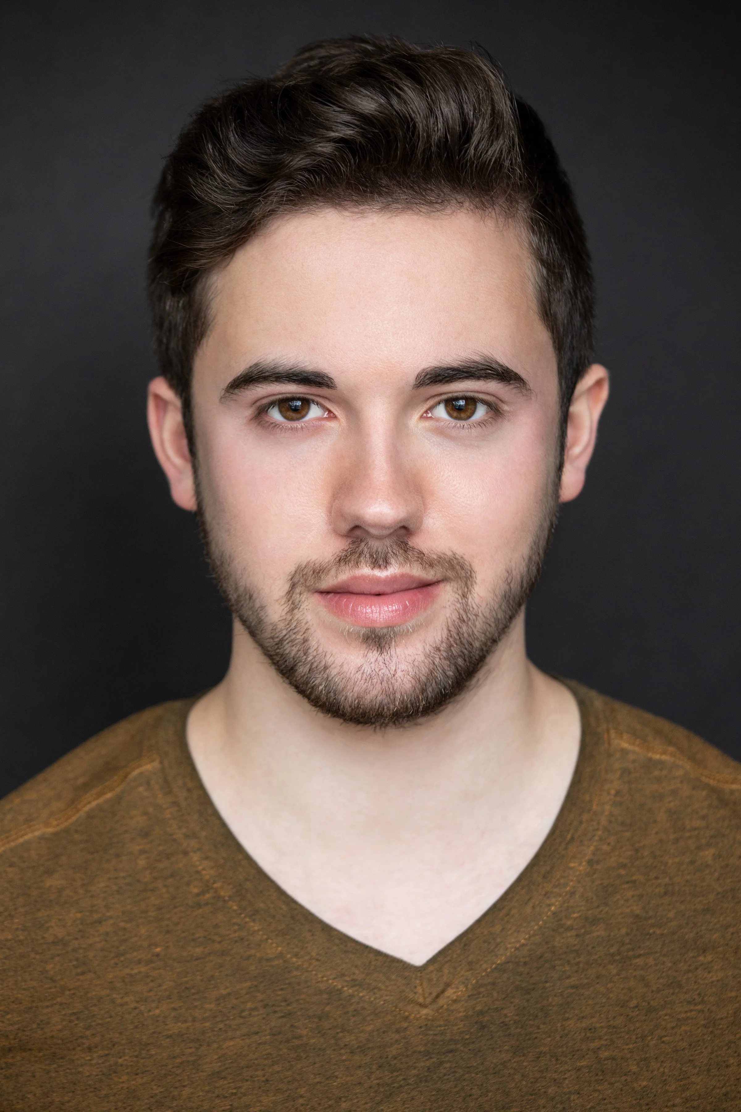 Kenneth Johnson, a white man, standing in front of a dark background. He has brown hair and a tidy beard. He is looking at the camera with an open expression, and is wearing a brown shirt.