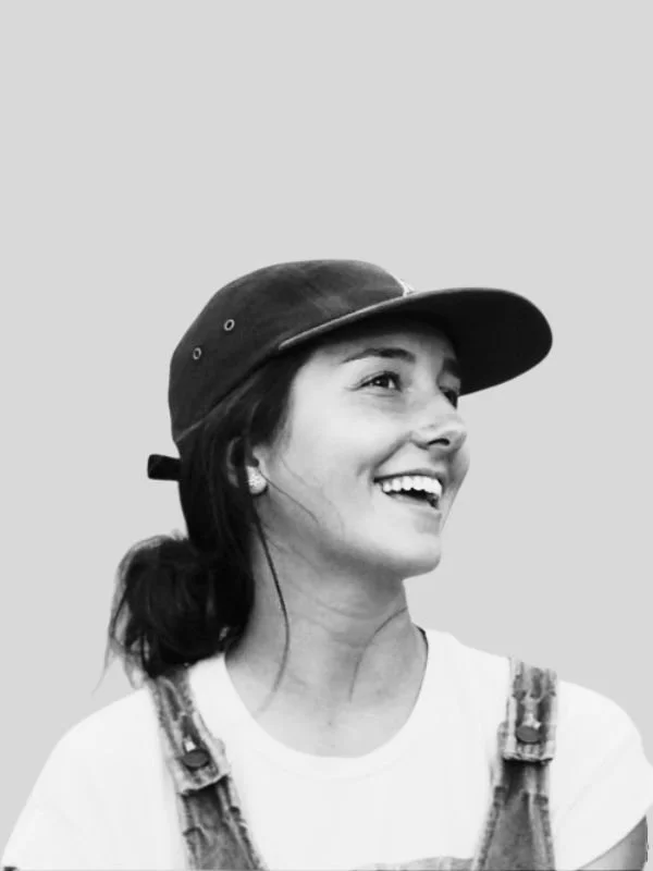 Michelle Austin smiling, wearing a baseball cap, earrings, a white T-shirt, and overalls.
