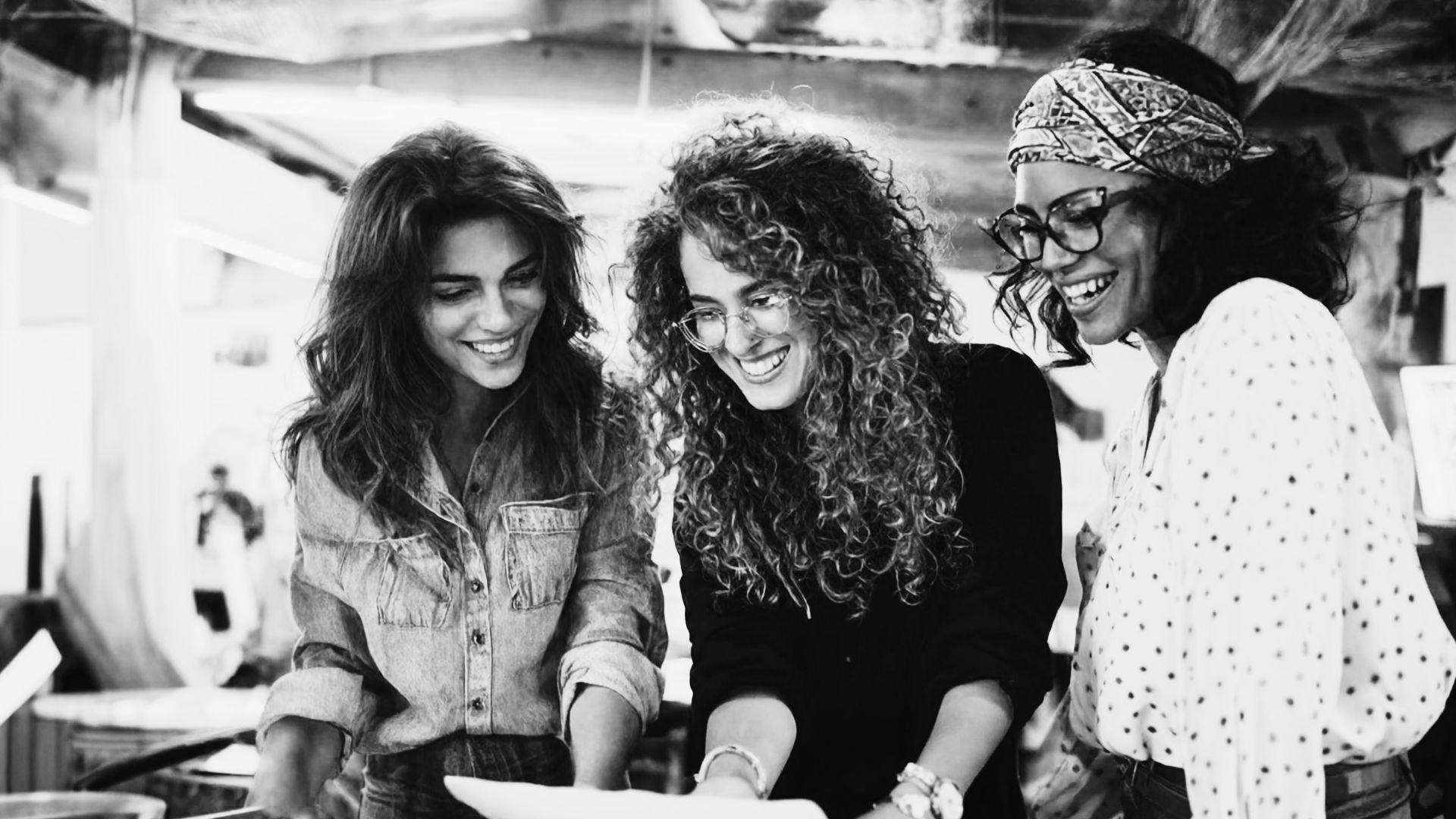 Three women smiling and looking at something together indoors.