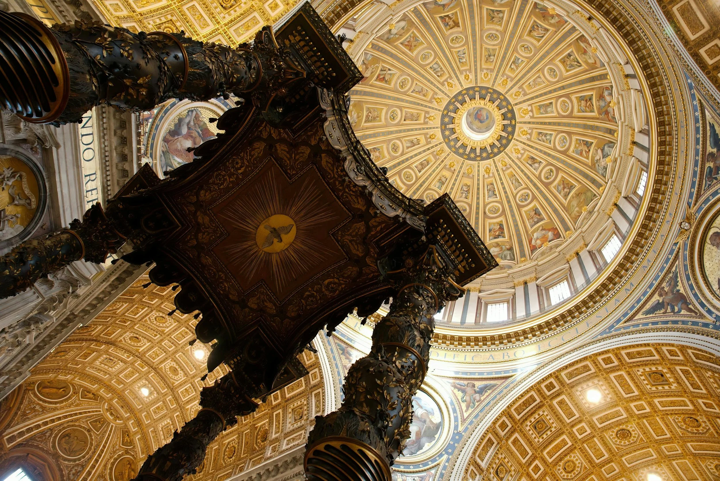 Interior view of a grand cathedral dome with intricate gold and painted designs, and a central ornate pulpit below.