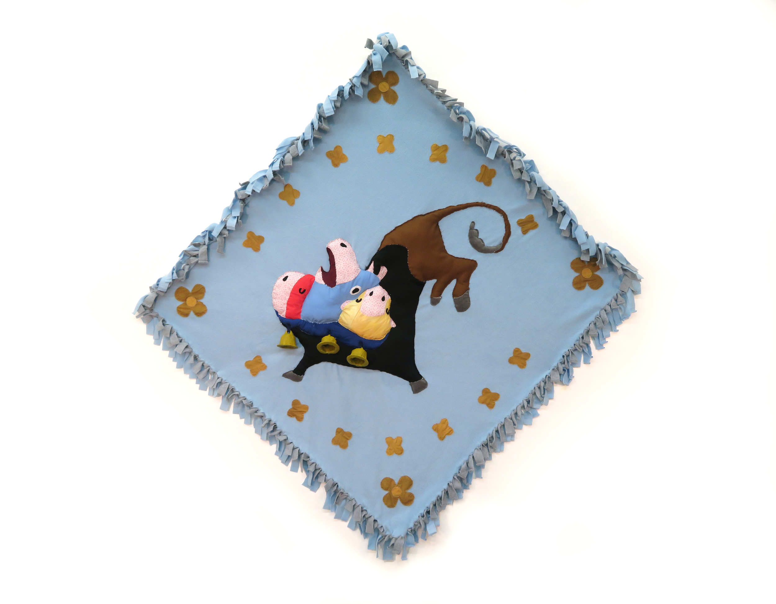 Felt artwork of a three headed cow, surrounded by patterned mustard flowers, on a light blue background with ruffled edges.