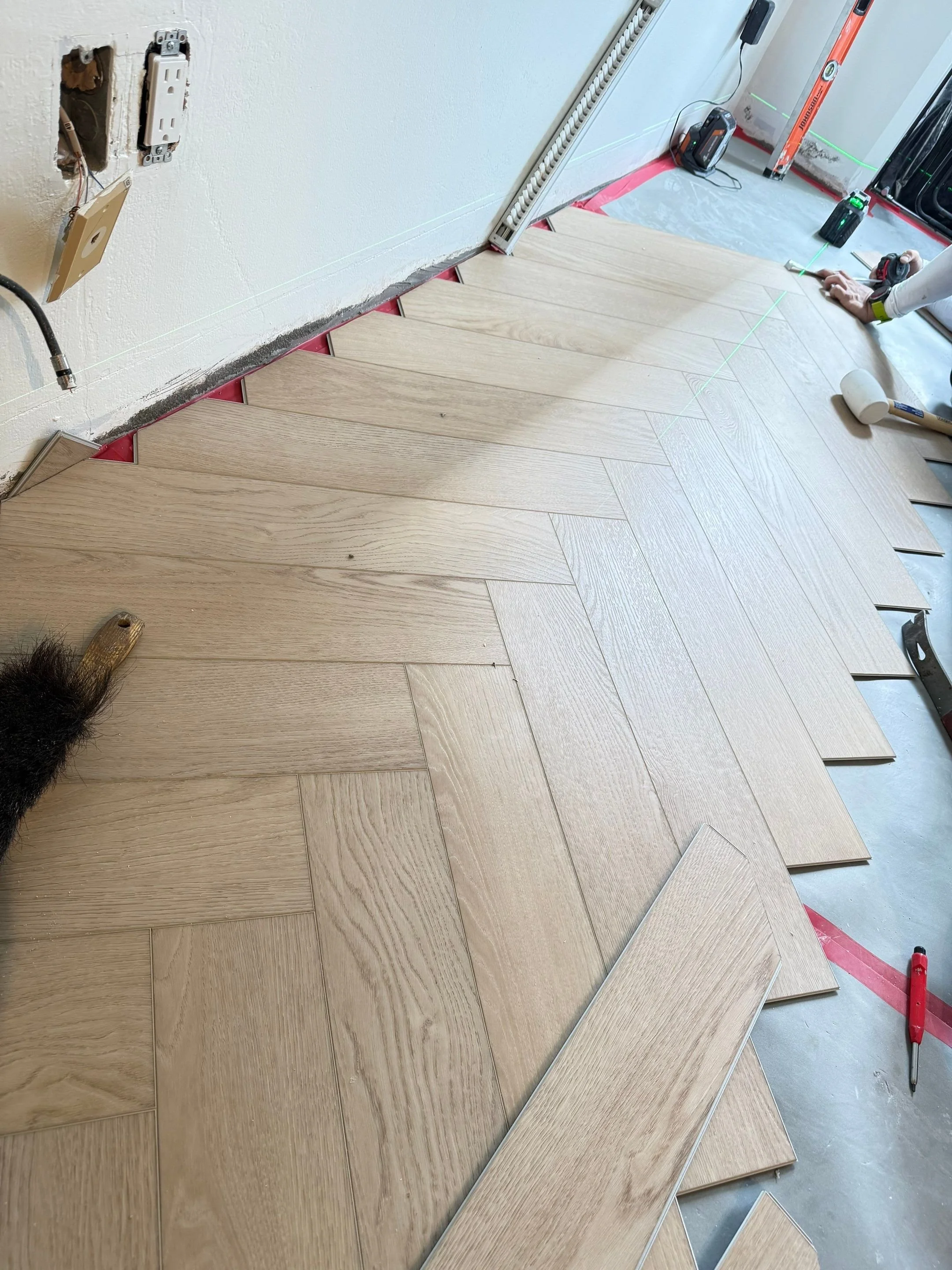Worker installing vinyl plank flooring with a laser guide, herringbone pattern, at a waikiki condo renovation.