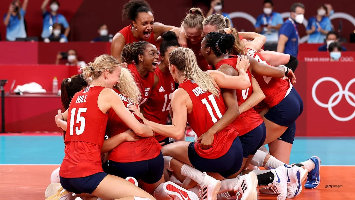 A group of female volleyball players in red jerseys celebrating together on the court during the Olympics.