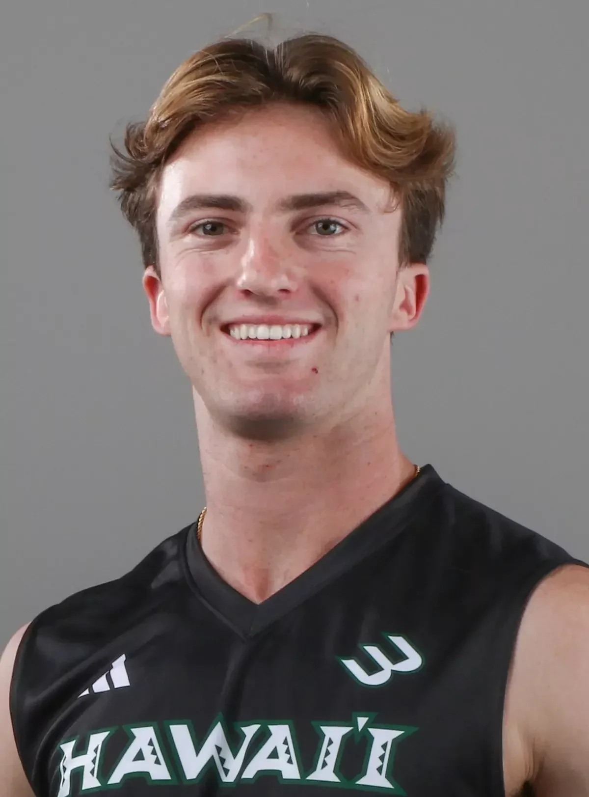 Young man smiling, wearing a black sports jersey with 'HAWAII' written on it, against a plain gray background.