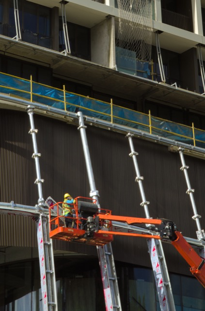 Construction worker in yellow helmet operating equipment on a crane at a building site