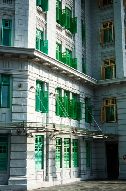 Exterior of a historic building with ornate architecture, multiple green and yellow window shutters, and fire escape cables.