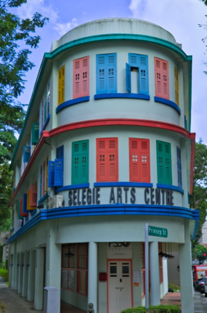 Colorful three-story building with rounded corners, featuring multiple windows with colorful shutters, and a sign that reads "Selegie Arts Centre."