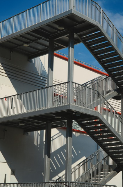 Exterior metal fire escape staircase on the side of a building with shadows cast by the railings