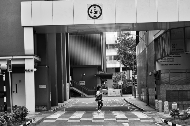 A person walking through an urban street under an overpass with a height restriction sign of 4.5 meters.