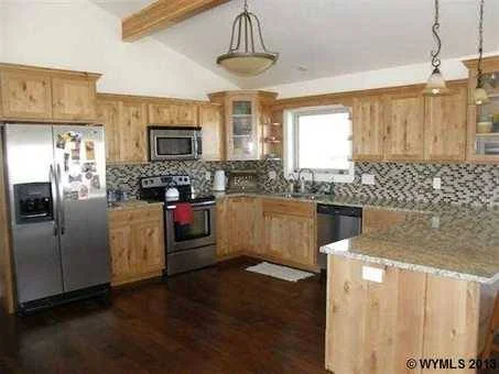 Kitchen with wooden cabinets, stainless steel refrigerator, stove, microwave, and granite countertops, with a patterned tile backsplash and a window above the sink.