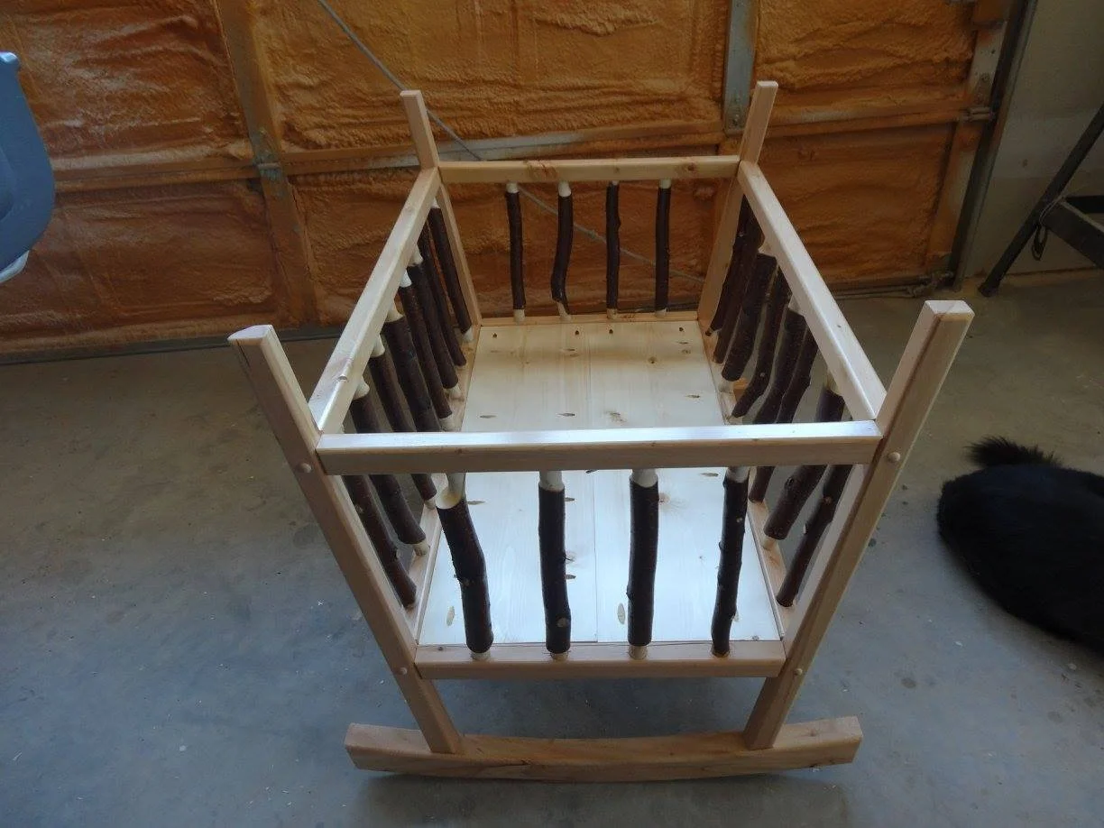 Wooden crib frame with black log-style vertical slats and a light wood base in a garage or workshop.