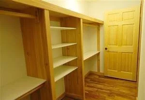 Empty wooden shelving unit with multiple glass shelves in a room with hardwood floors and a closed wooden door.