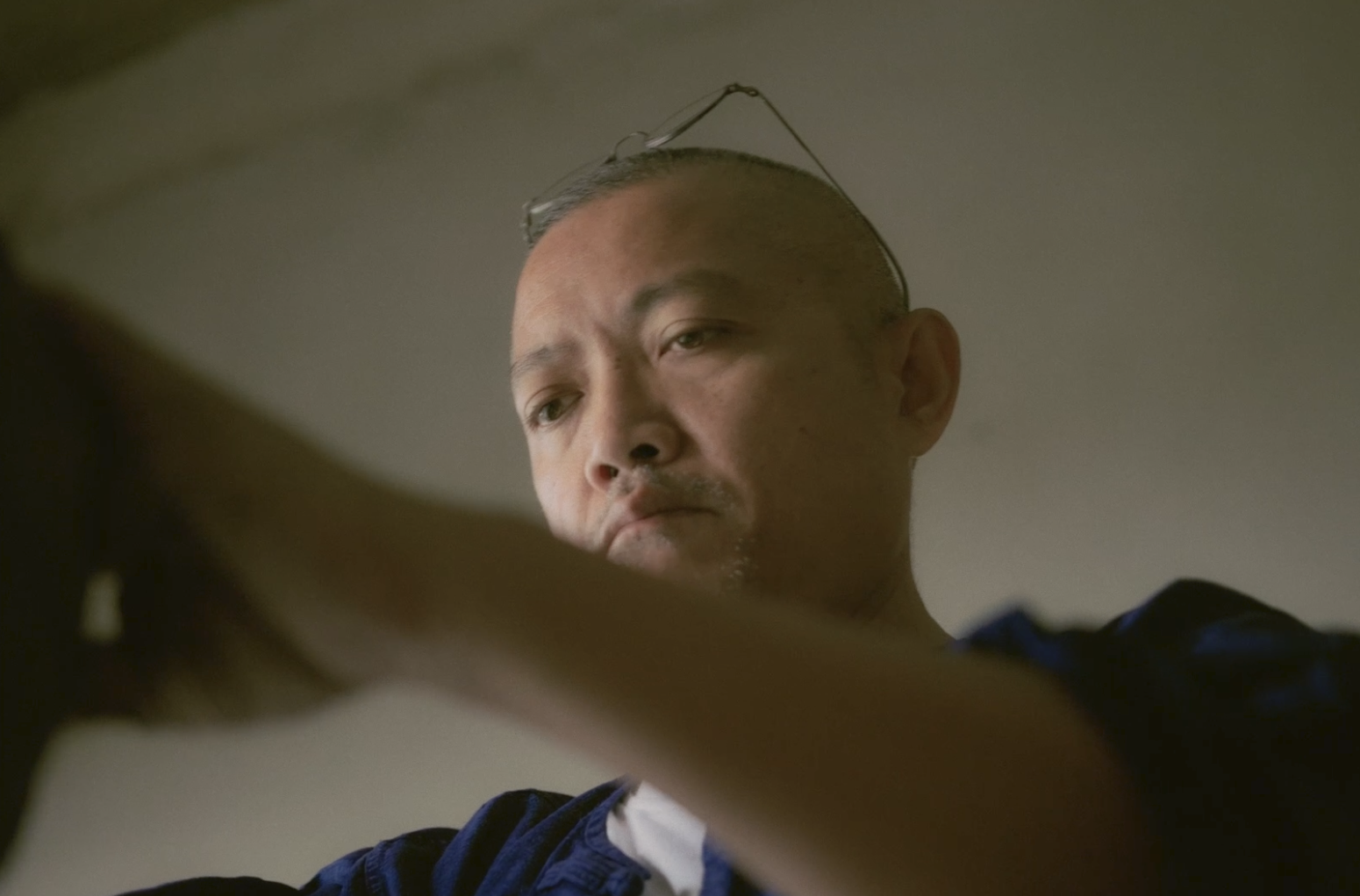 A man with a shaved head looking down at something, with glasses resting on his head and a serious expression.