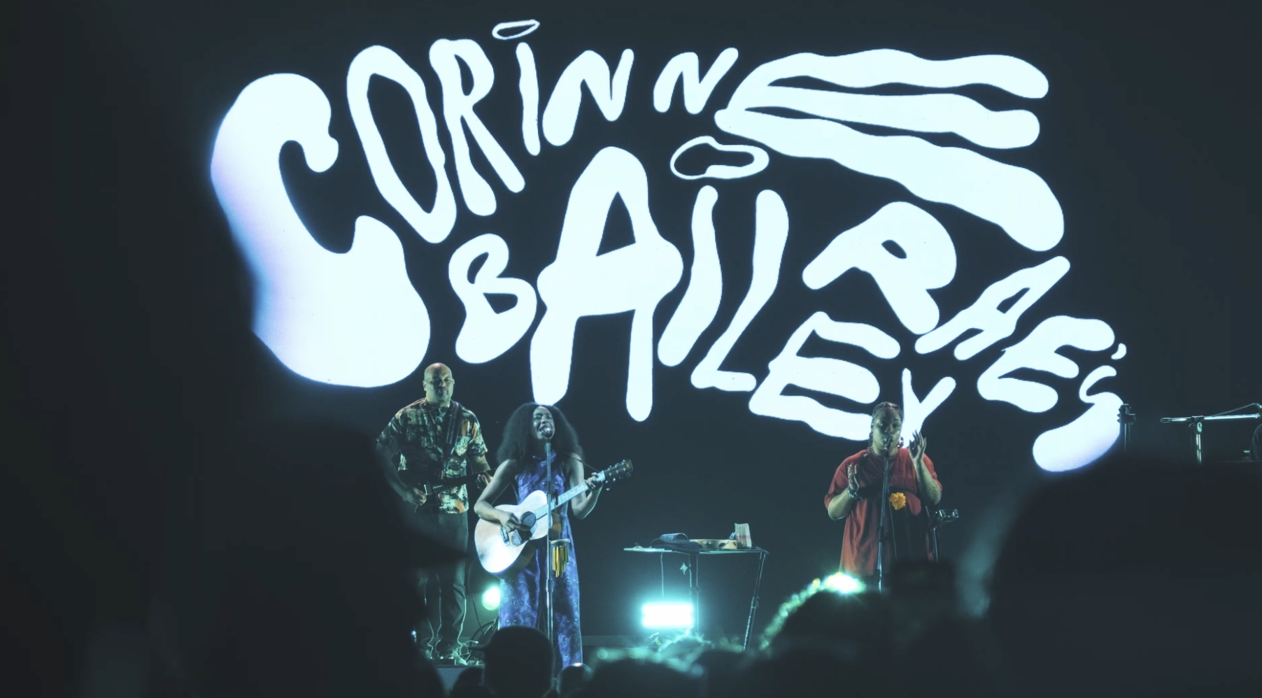 Musicians performing on stage with a large screen displaying the phrase 'Sorrindo é Básico' behind them. Concert and music event