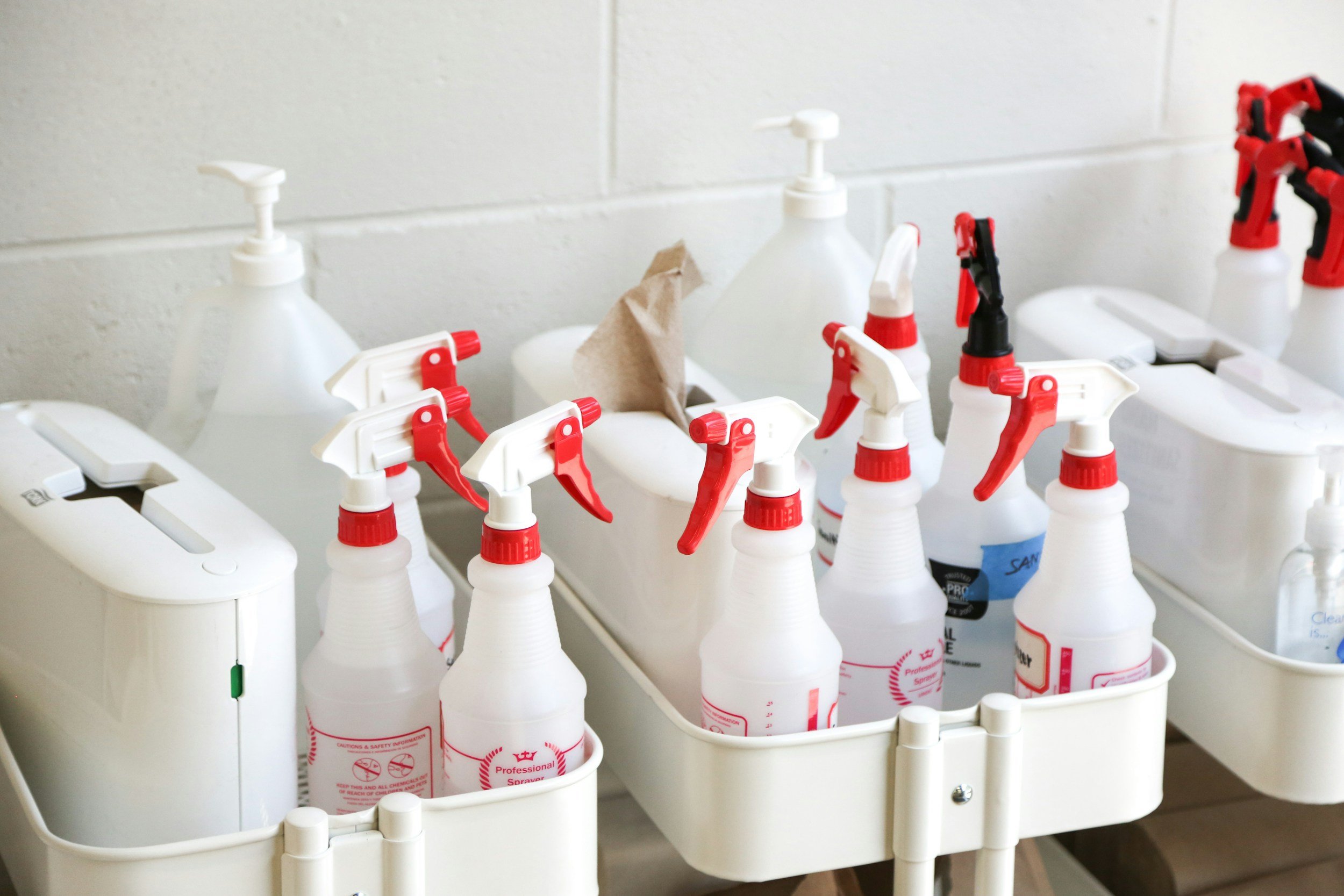 Collection of spray bottles, hand sanitizer dispensers, and cleaning supplies stored in a white plastic organizer.
