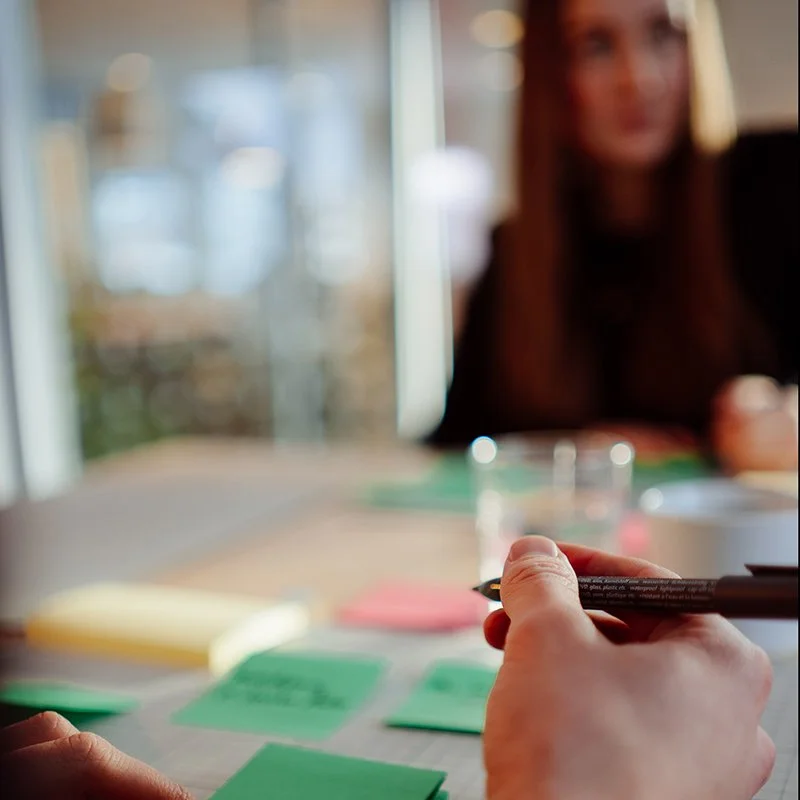 to hender som skriver på post it-lapper i en workshop med ung kvinne blurred i bakgrunnen