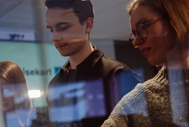 tre personer i workshop bak en glassvegg