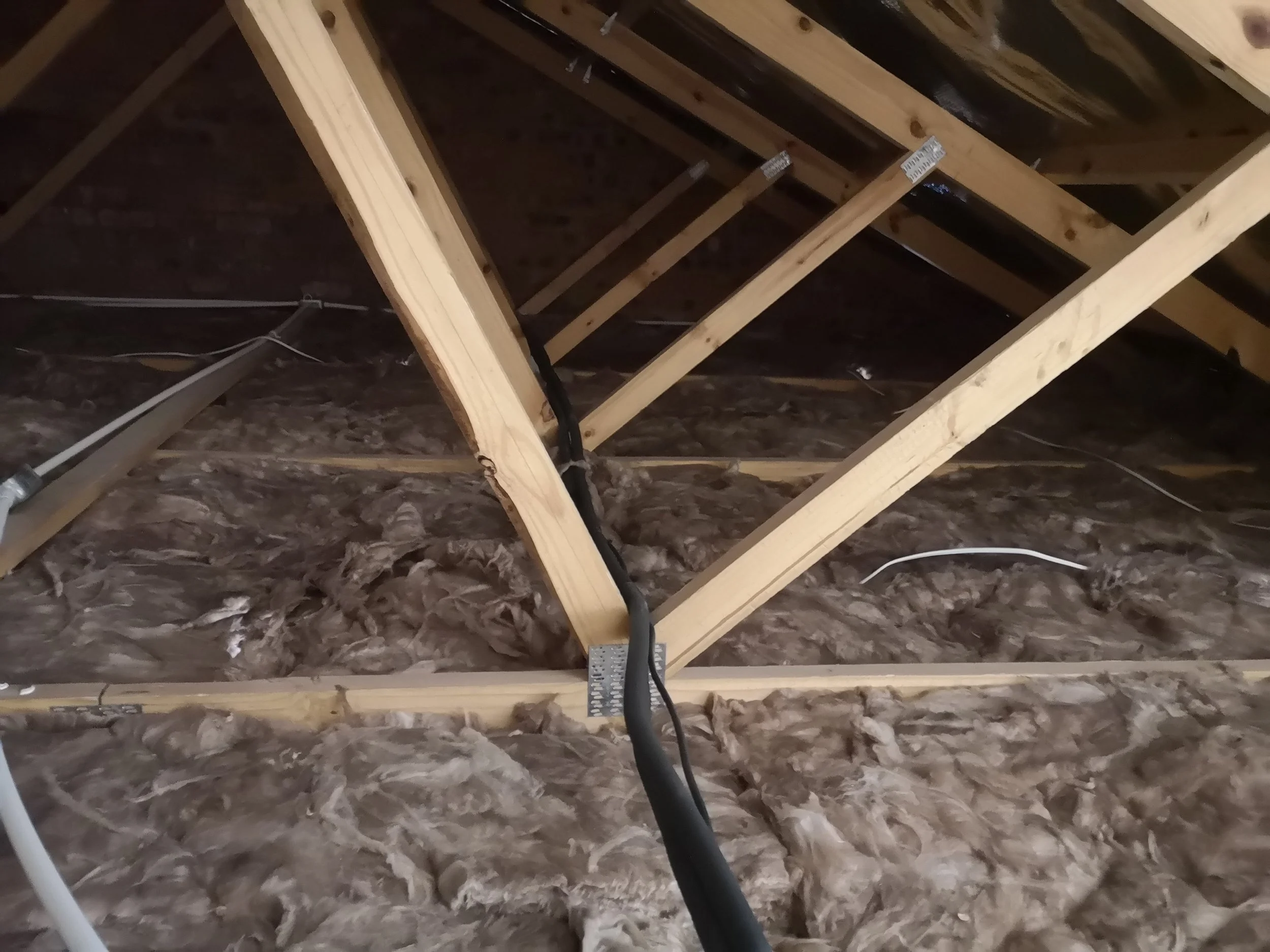 View of an attic space with exposed wooden framing, insulation, and electrical wiring.