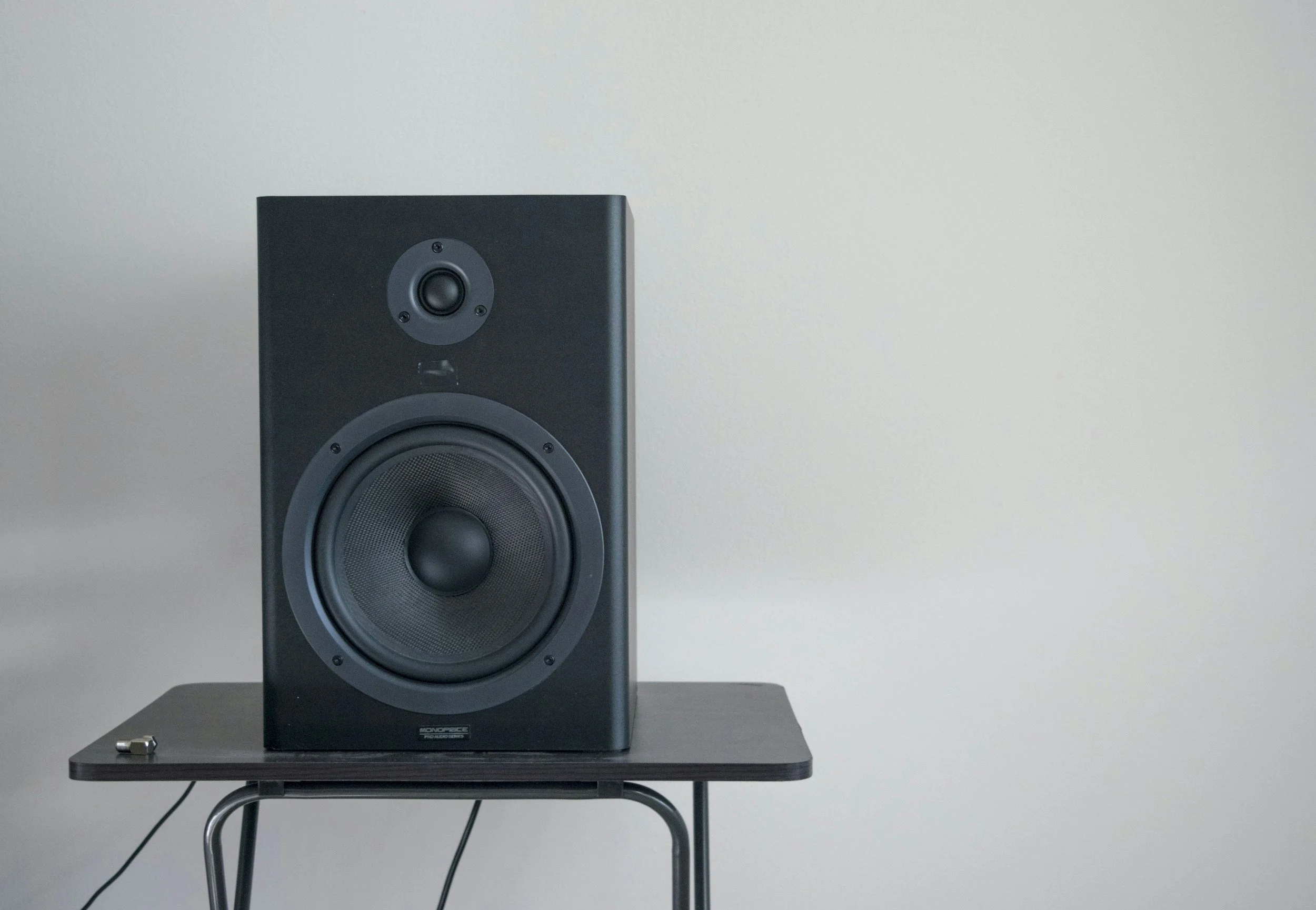 Black speaker on a small wooden table against a white wall.