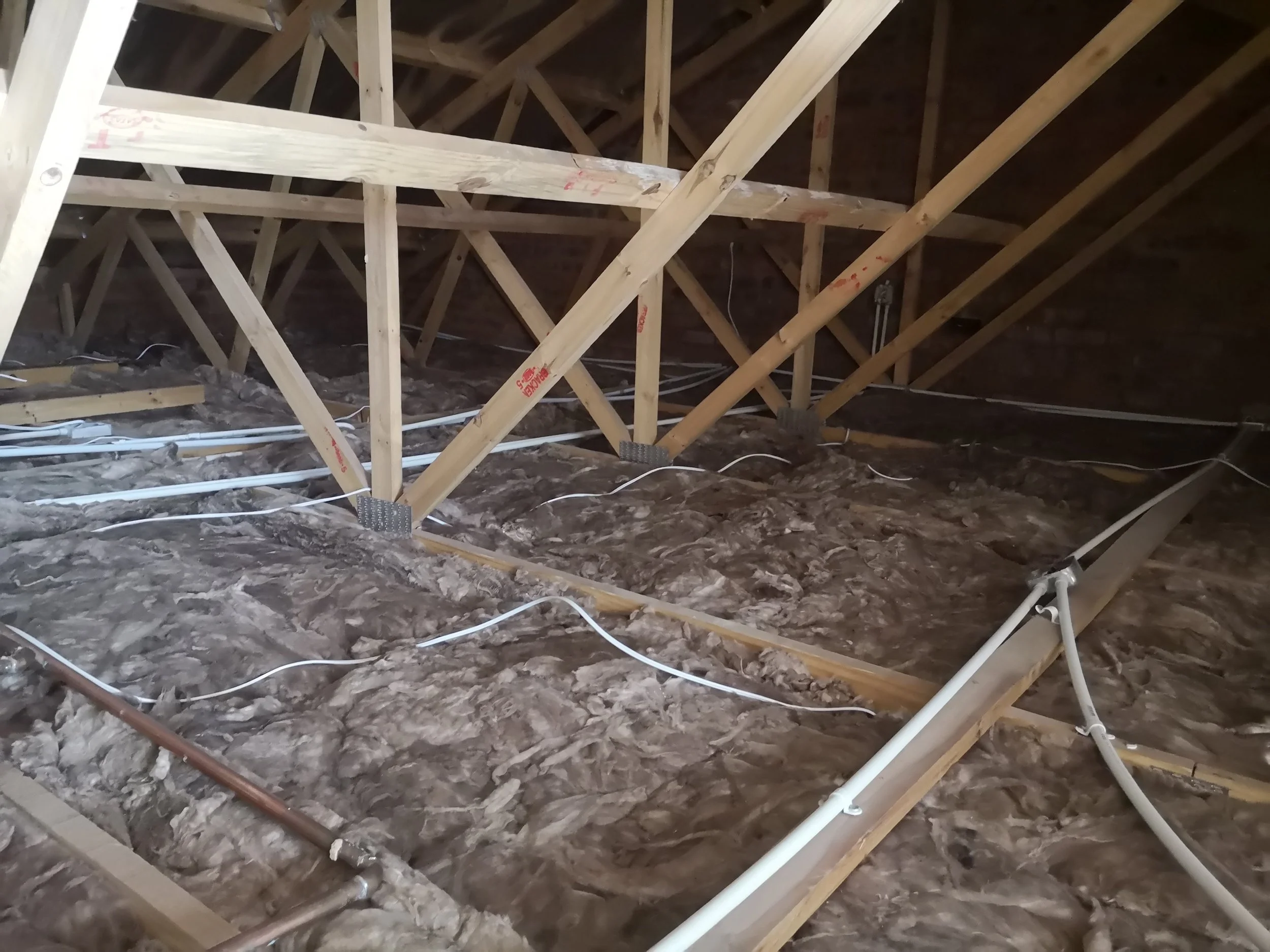 Interior view of an attic under construction, showing wooden framing, insulation, and electrical wiring.