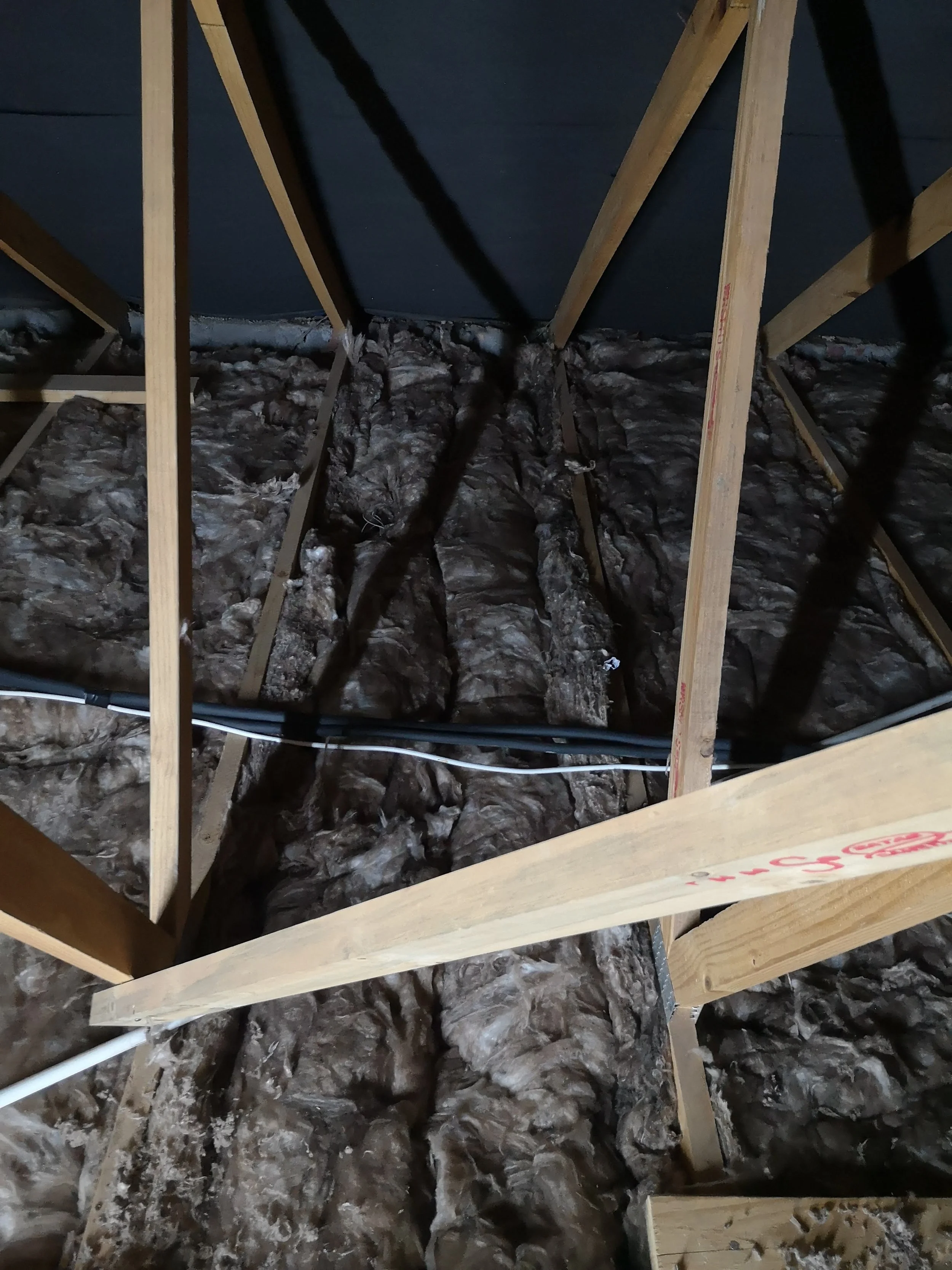 View of an attic with exposed insulation, wooden framing, and electrical wiring.