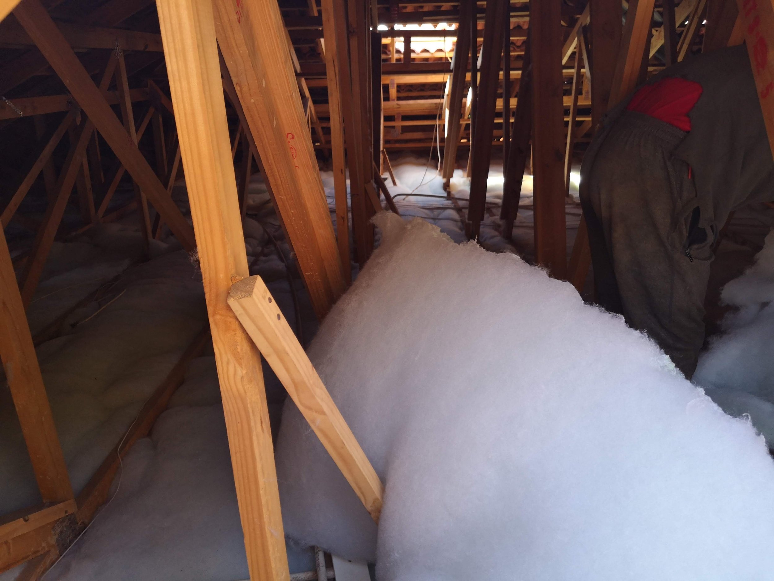 A person working in an attic with exposed wooden beams, surrounded by insulation material.