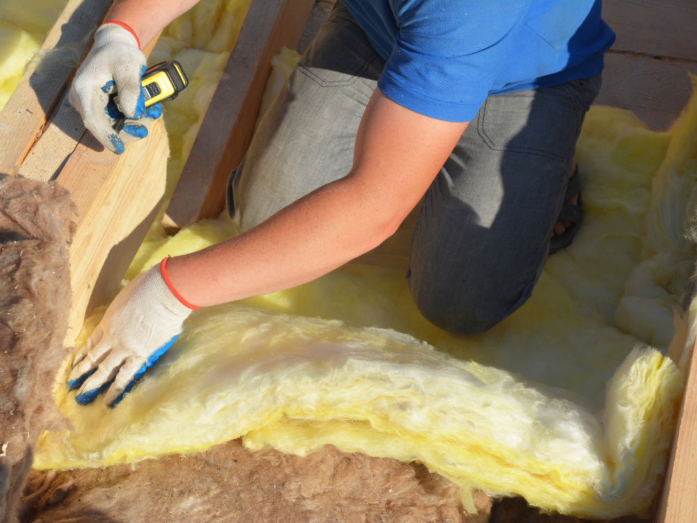 A person installing insulation in a building, wearing gloves and kneeling on the floor.
