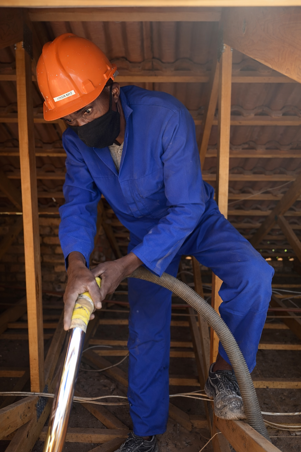 A construction worker in blue coveralls and an orange safety helmet using a vaccuum to clean roof