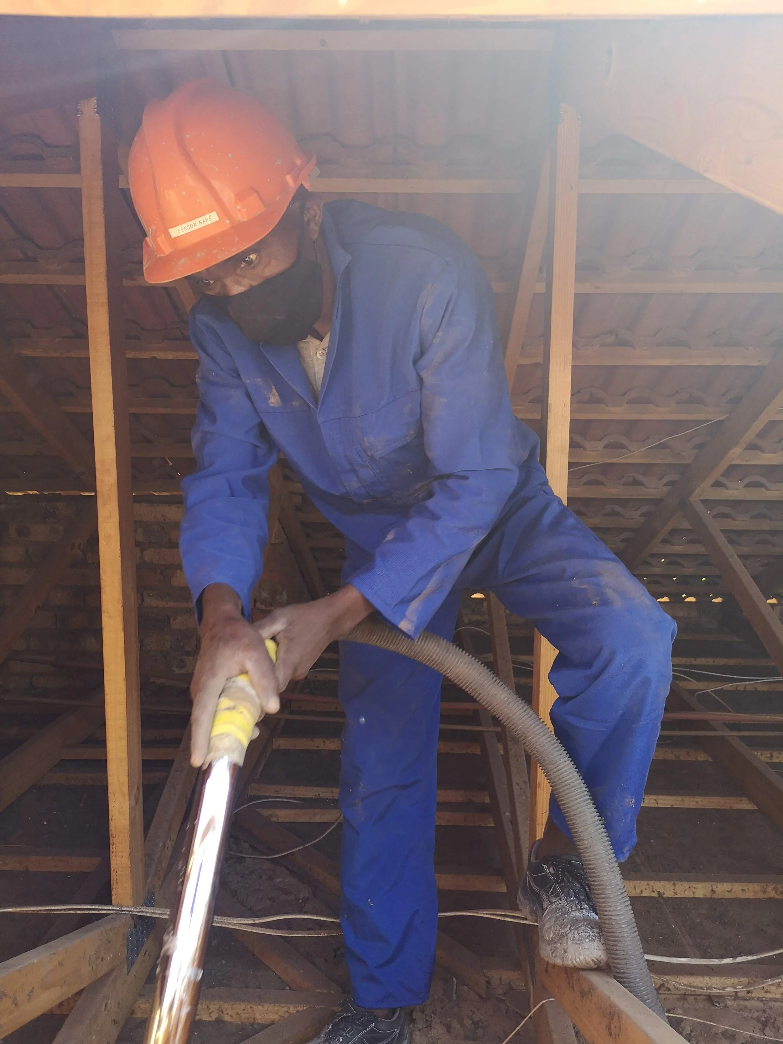 A construction worker in blue overalls vacuuming Roof - Ceiling Insulation Gauteng