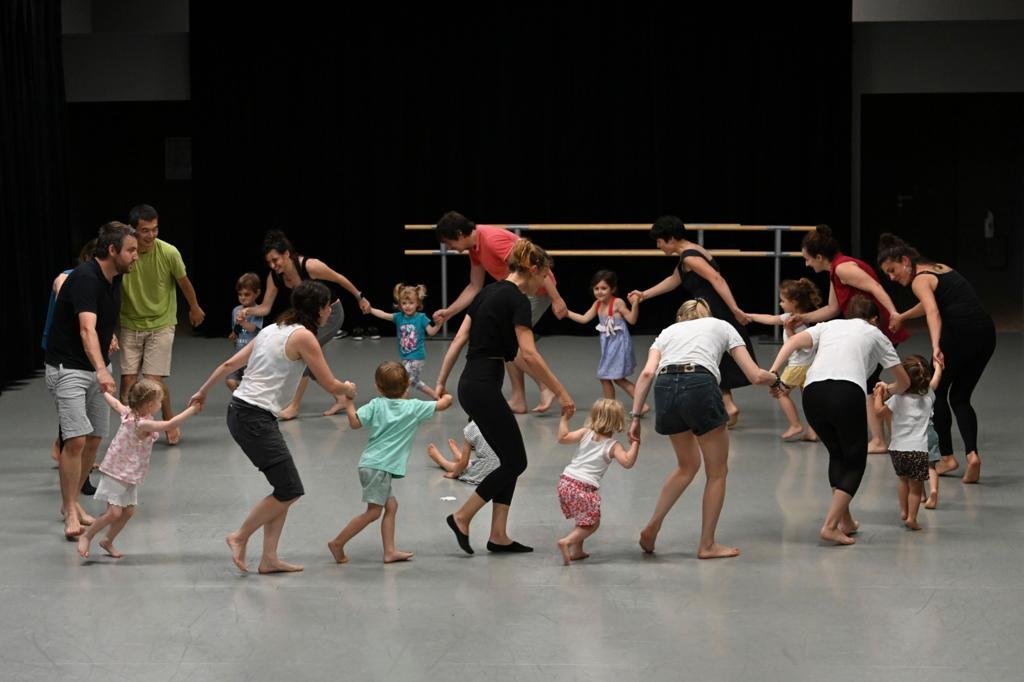 Adults and children dancing in a circle in a dance studio.