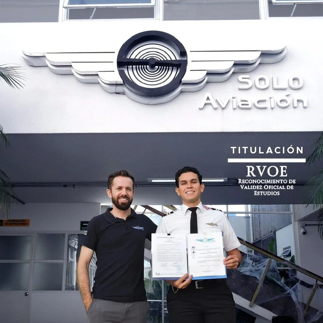 Dos hombres en uniforme de aviación frente a la entrada de un edificio con un signo que dice 'Solo Aviación', uno sostiene un certificado y ambos sonríen.