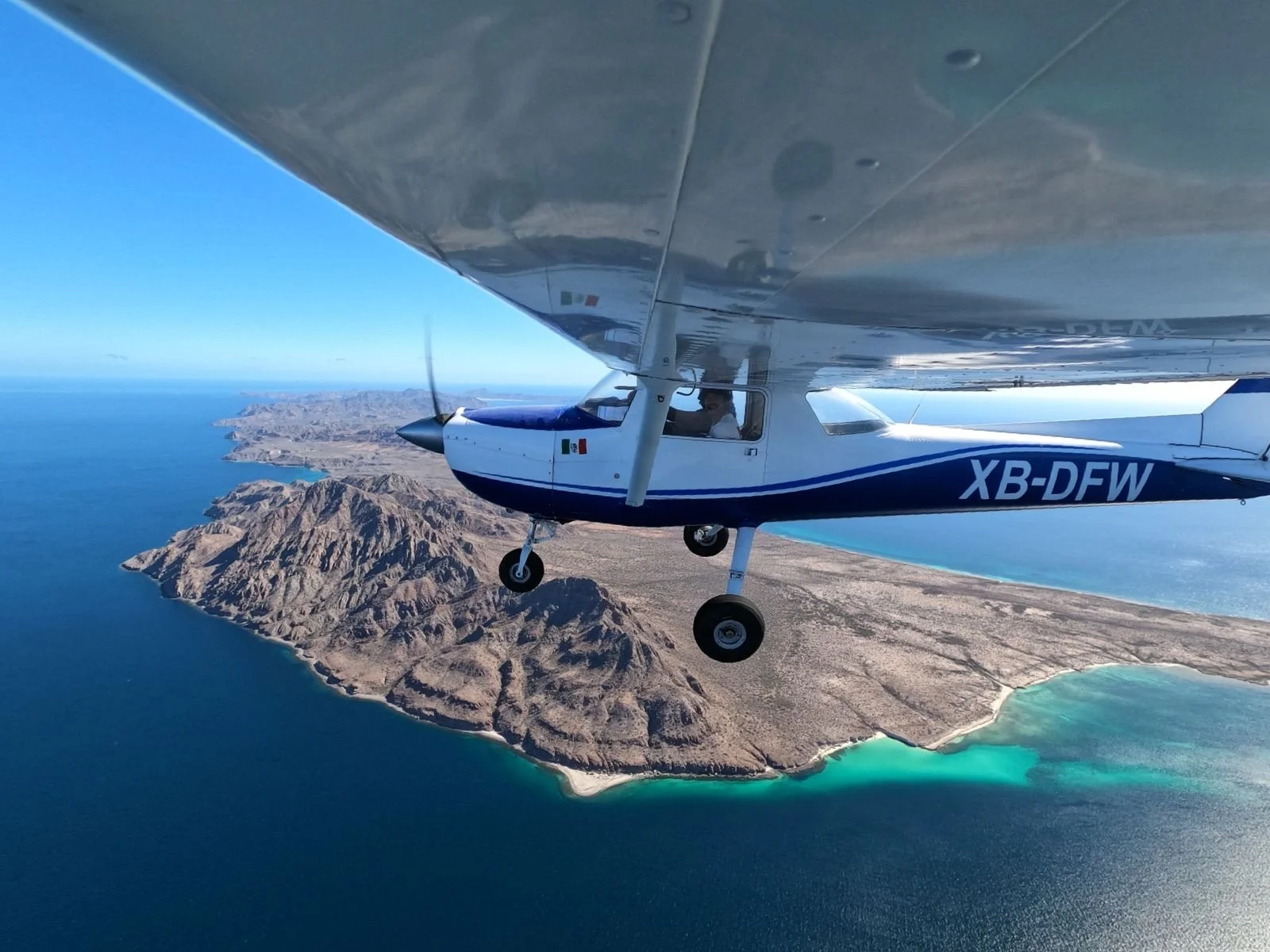 Avión pequeño sobre un paisaje costero con montañas y mar en un día despejado.