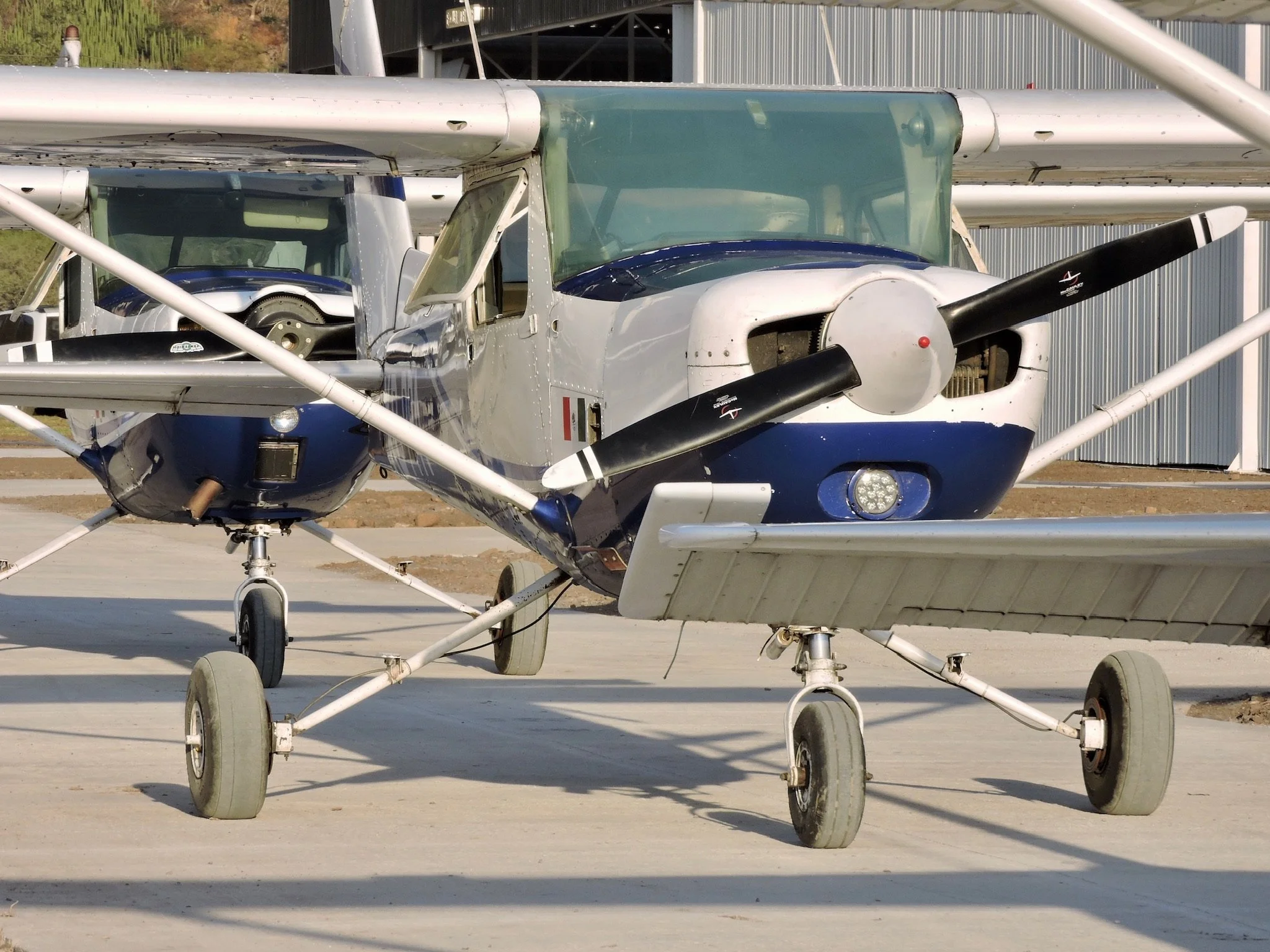 Avión de entrenamiento de pequeño tamaño estacionado en tierra, con hélice en la nariz y alas en la parte superior.
