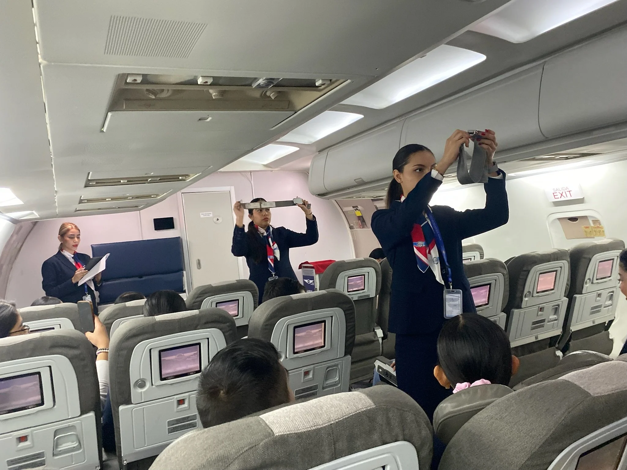 Tripulación de avión realizando la preparación antes del vuelo, con pasajeros sentados en sus asientos.