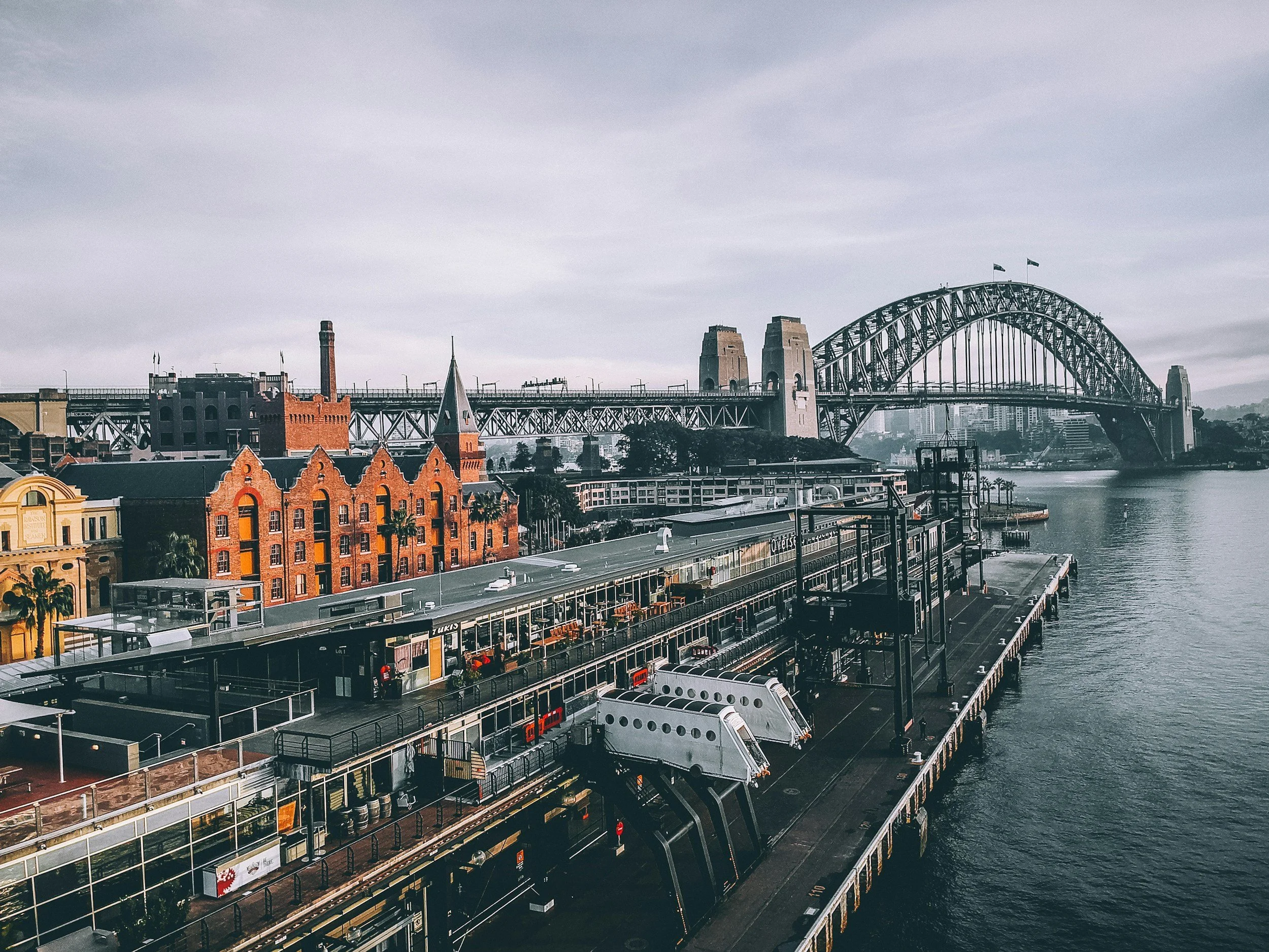 View of the Sydney Harbour Bridge with buildings in the foreground and an overcast sky.
