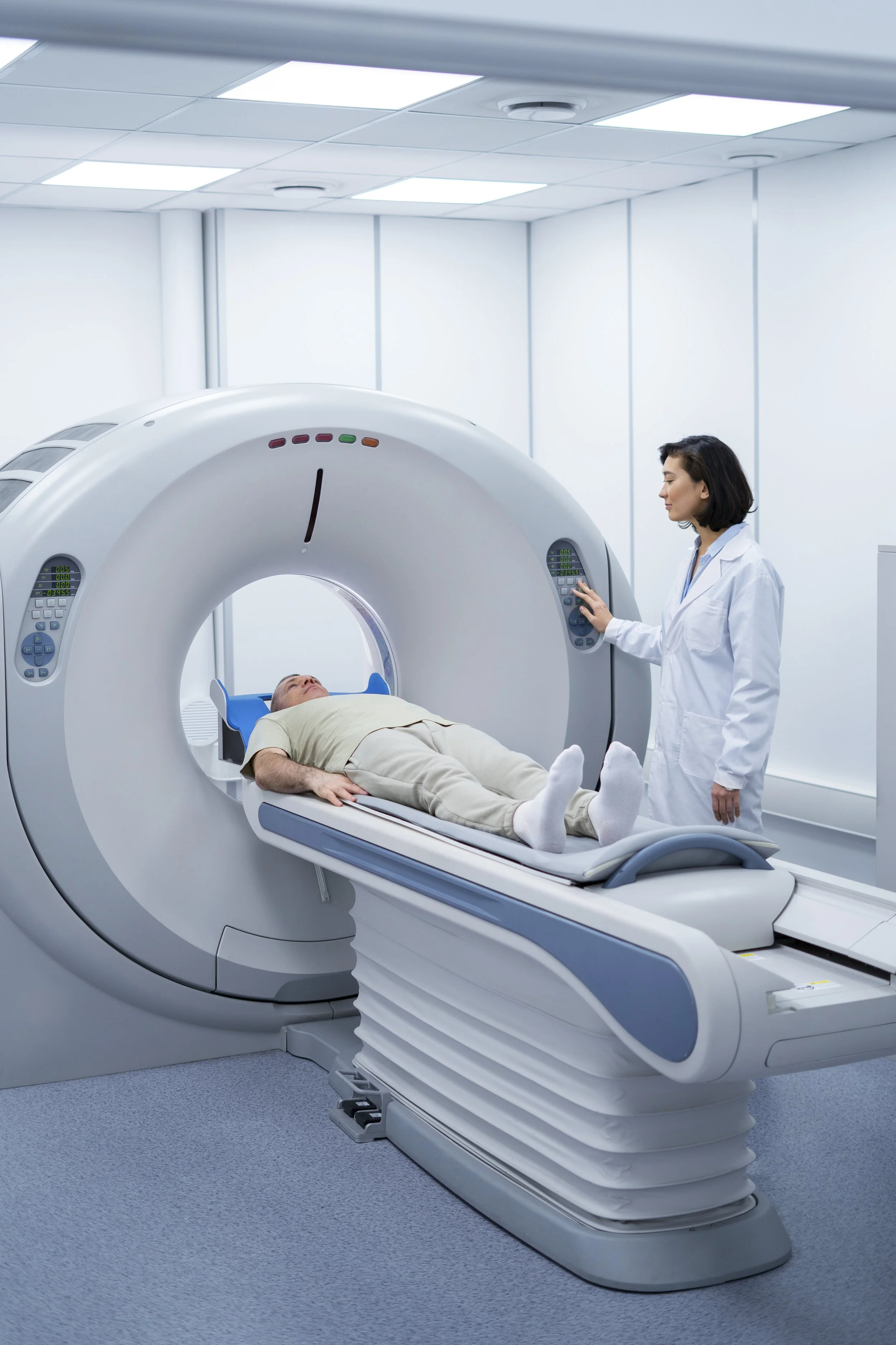 A patient lying on a medical scan table inside an MRI machine with a healthcare professional operating the controls.