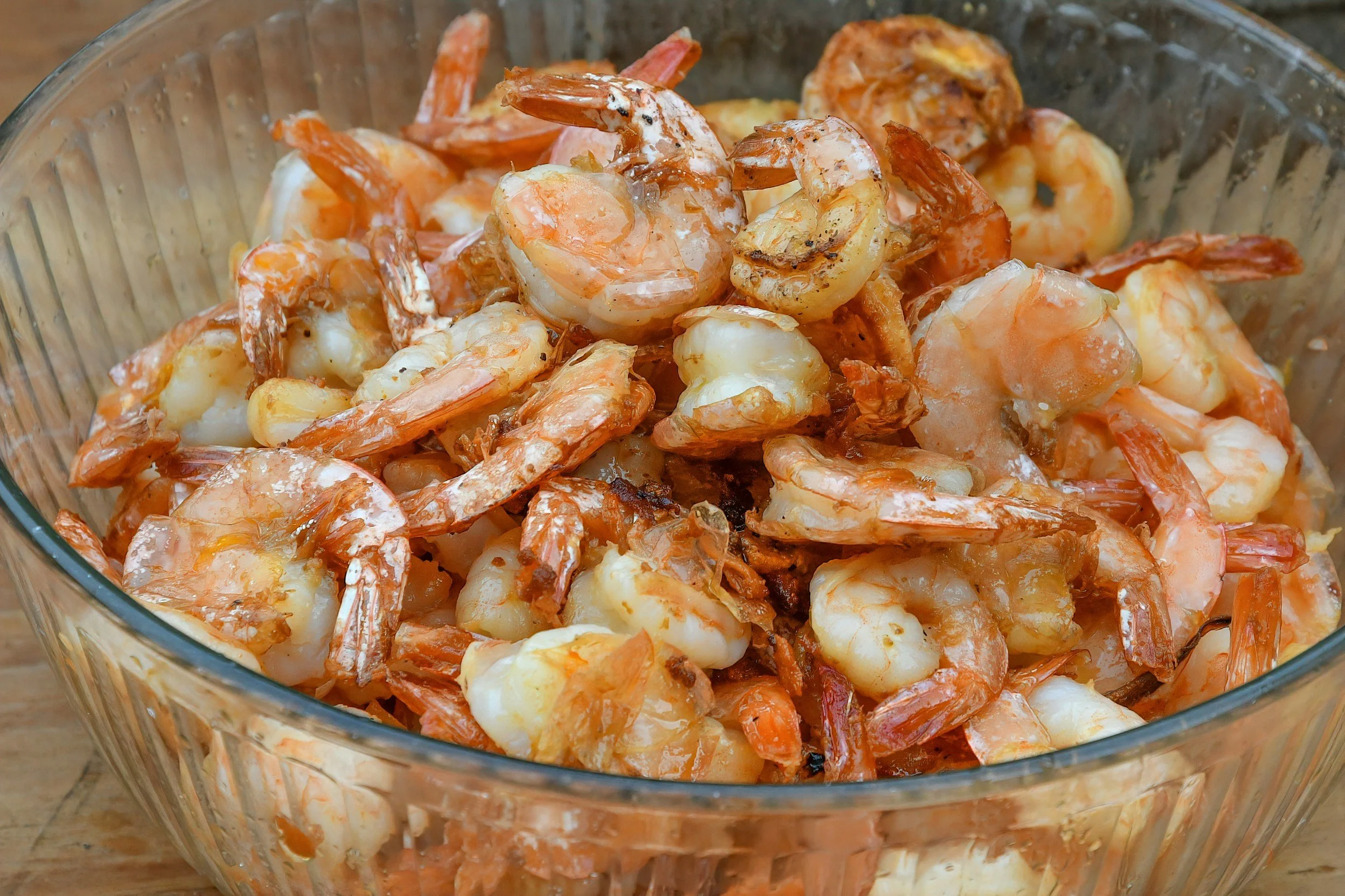 A glass bowl filled with cooked shrimp on a wooden surface.
