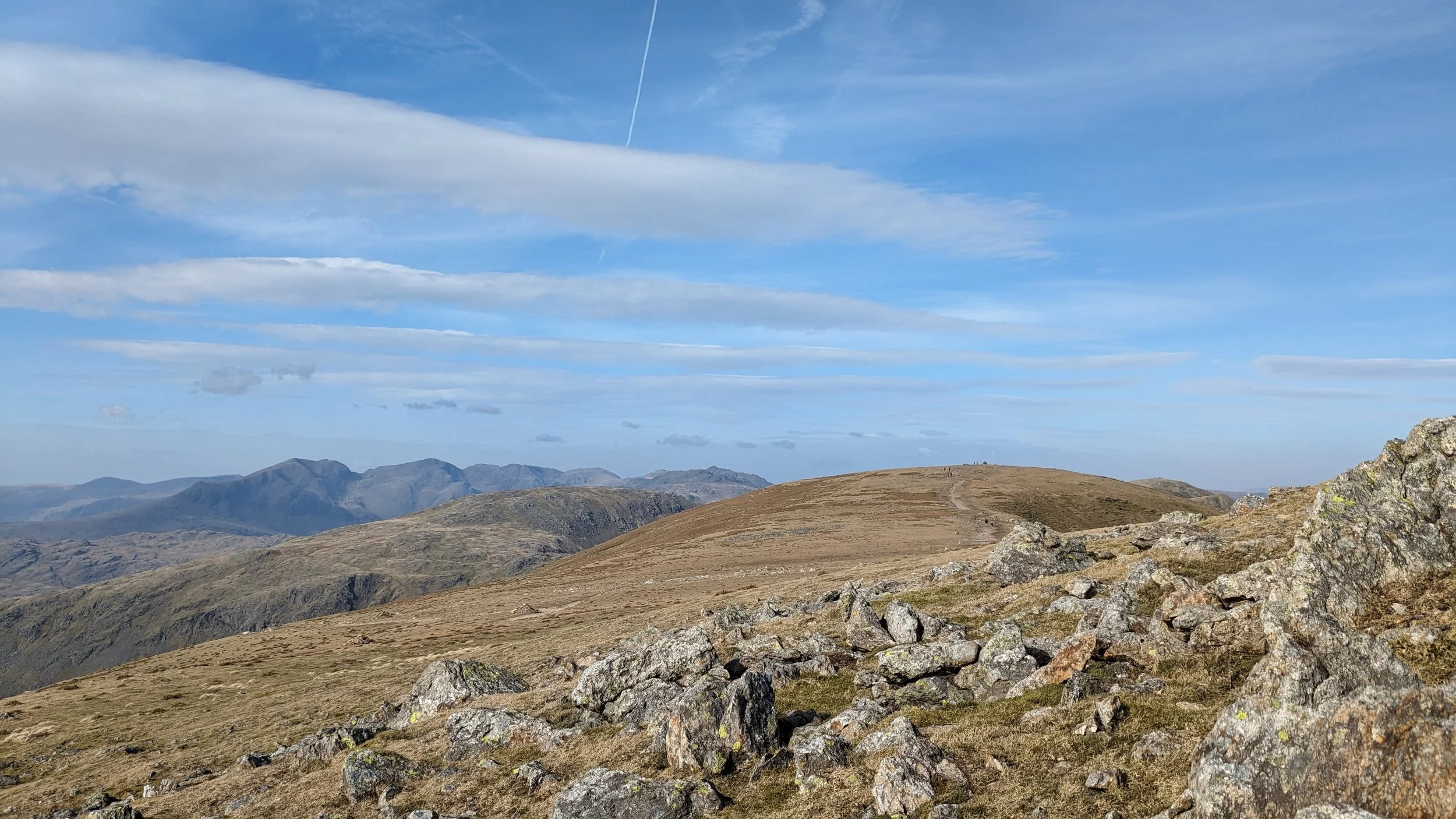 A sunny day in the UK Lake District rewards a hiker with views over a mountainous landscape