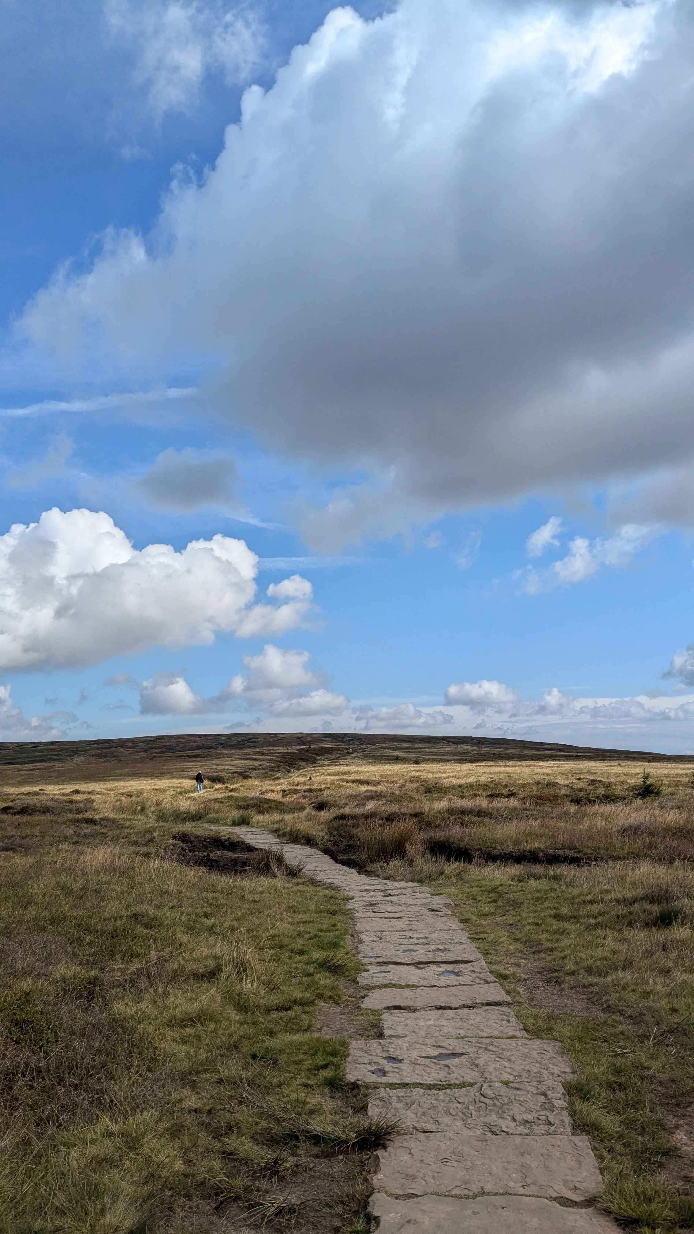 A hiker walks on a stone pathway across moorland in the UK Peak District.