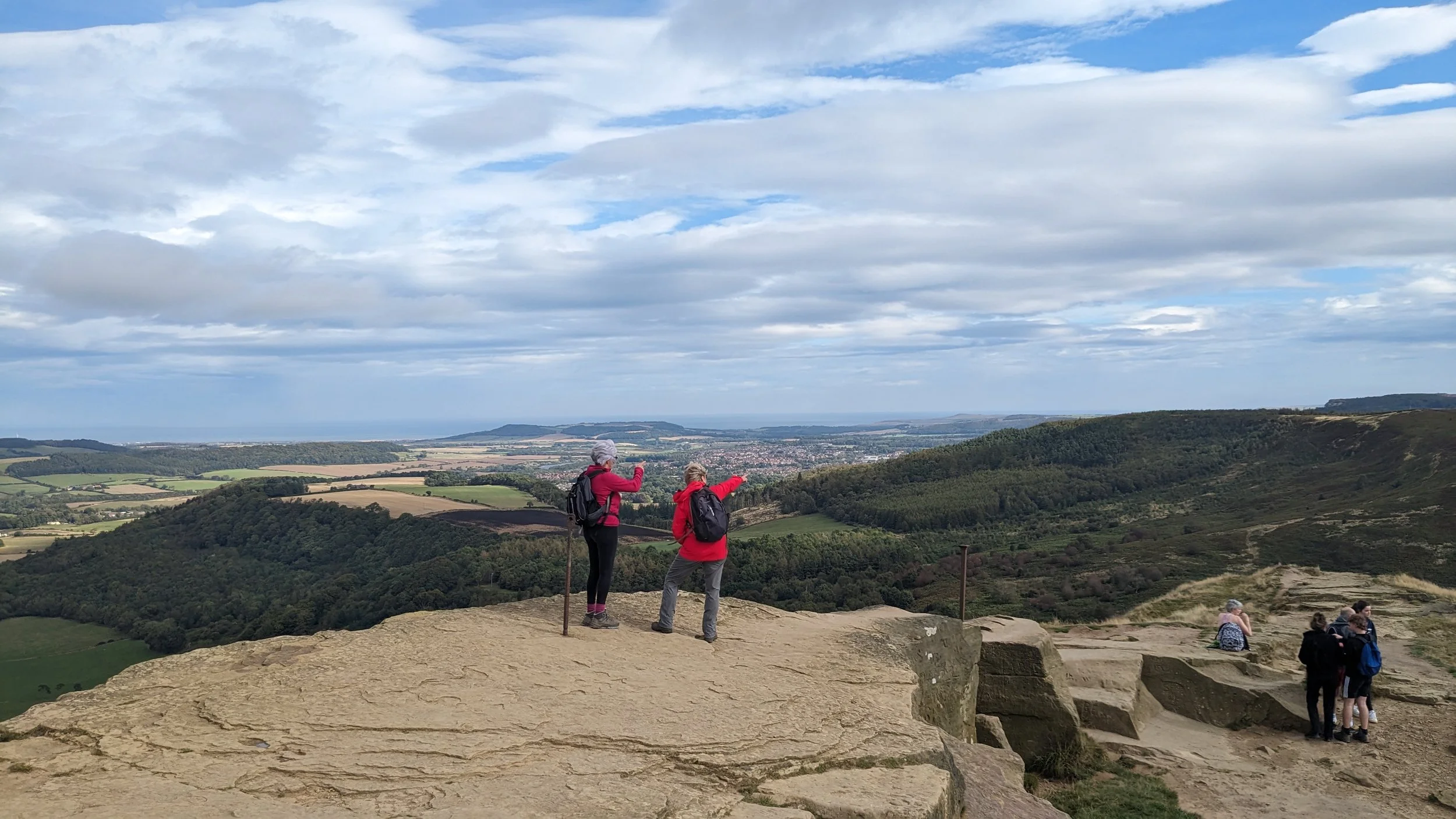 Women point at the distant landscape after hiking to the rocky summit of Roseberry Topping