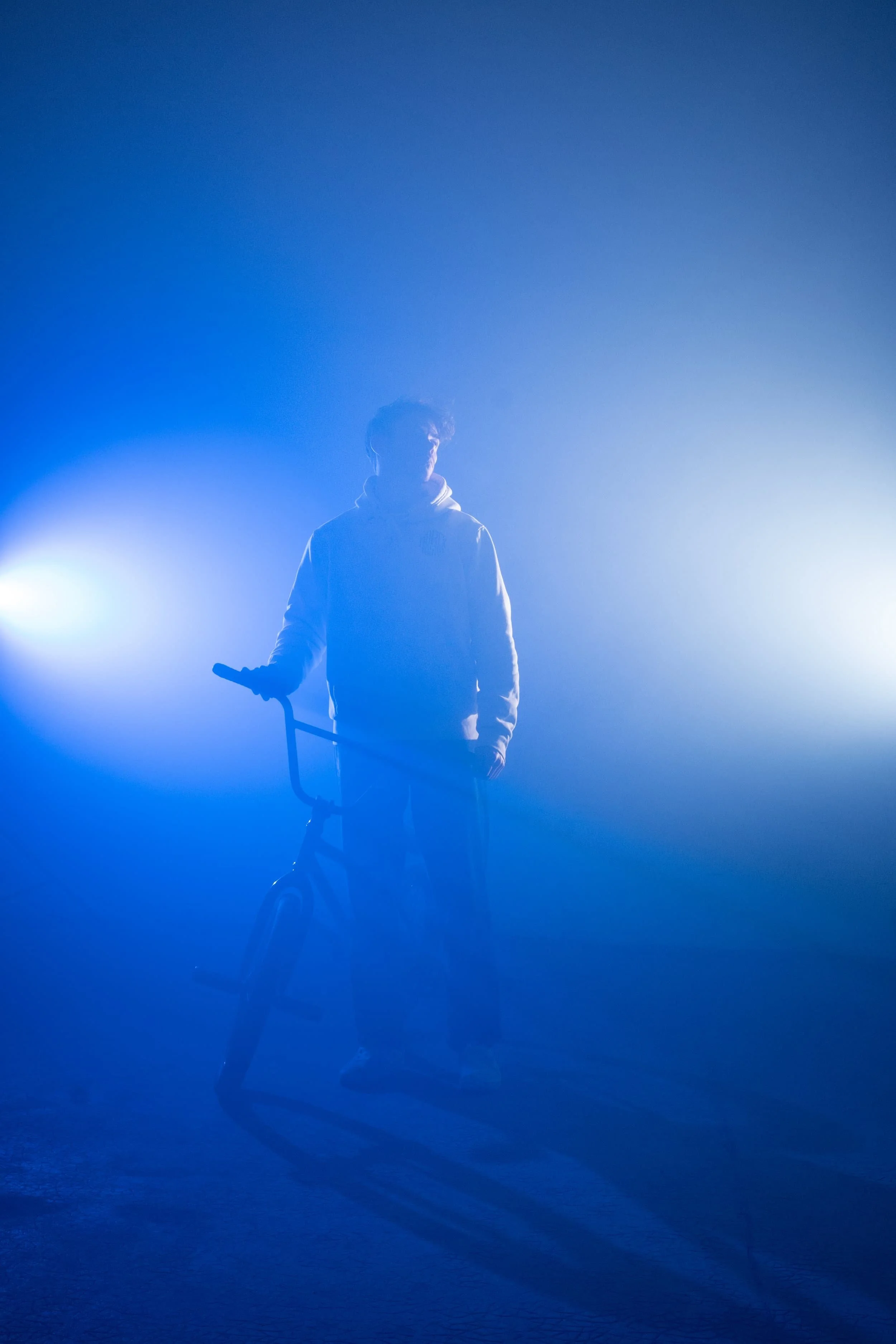 Anatole Rahain est entouré d'une lumière bleue douce et intense, en studio, à côté d'un vélo BMX
