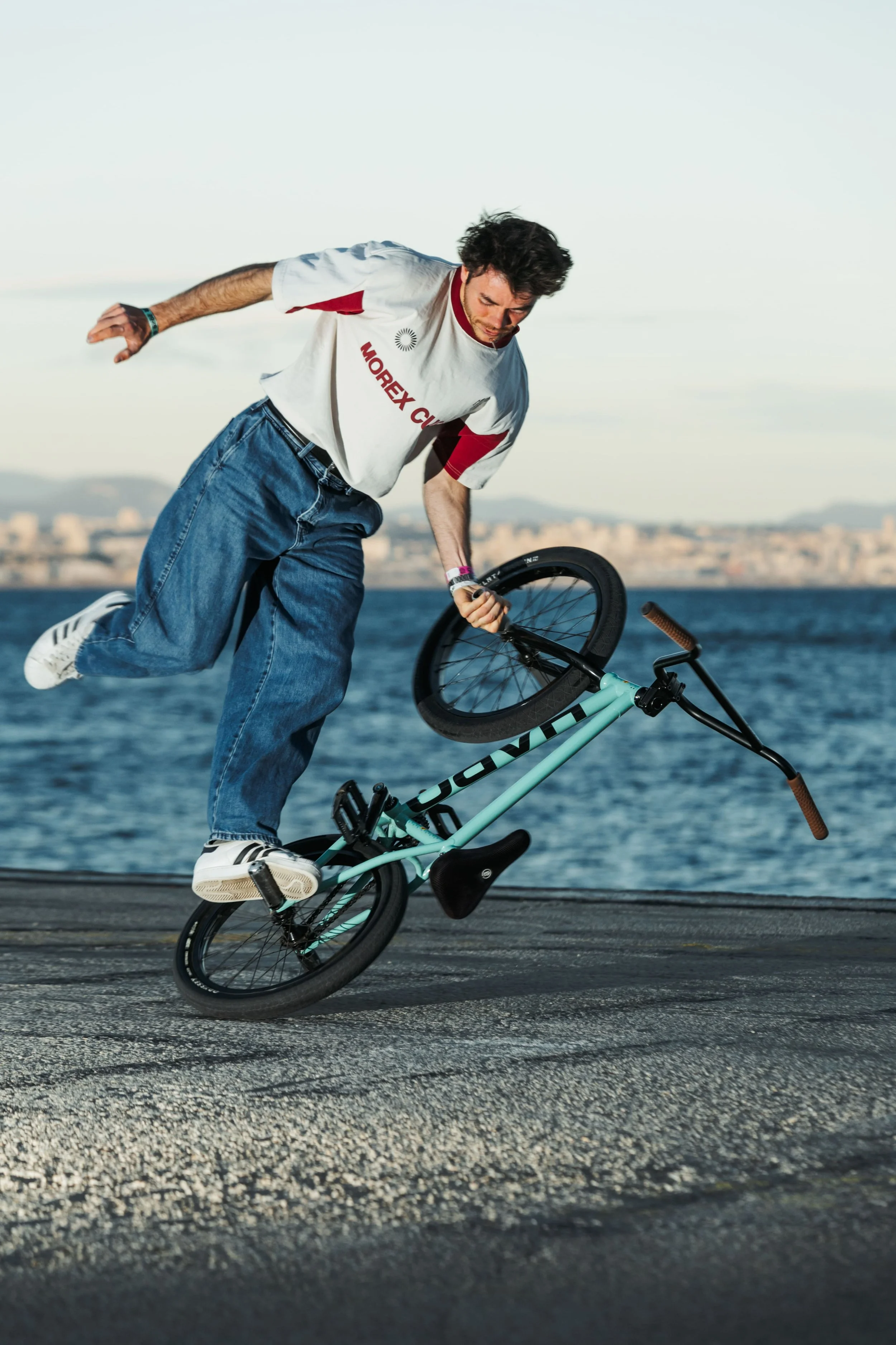Anatole Rahain en trick de BMX flat sur le quai en béton, la mer et les collines de Marseille en arrière-plan