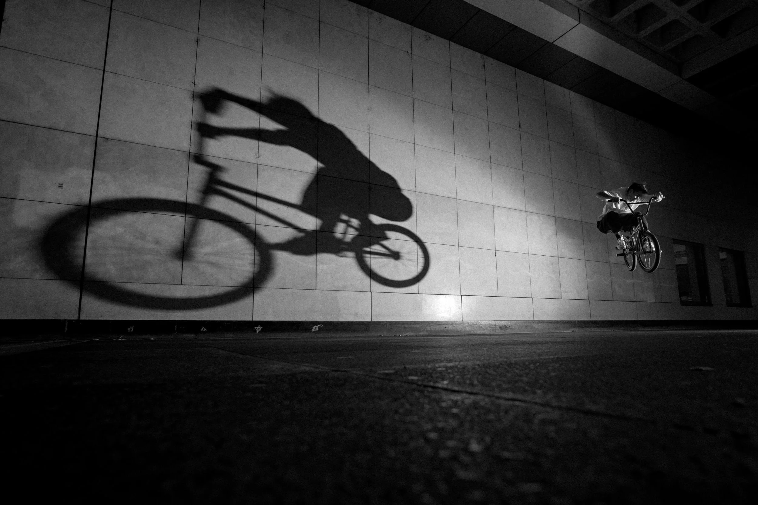 Anatole Rahain faisant du vélo, projetée en ombre sur un mur, vue de bas en haut dans un environnement sombre.