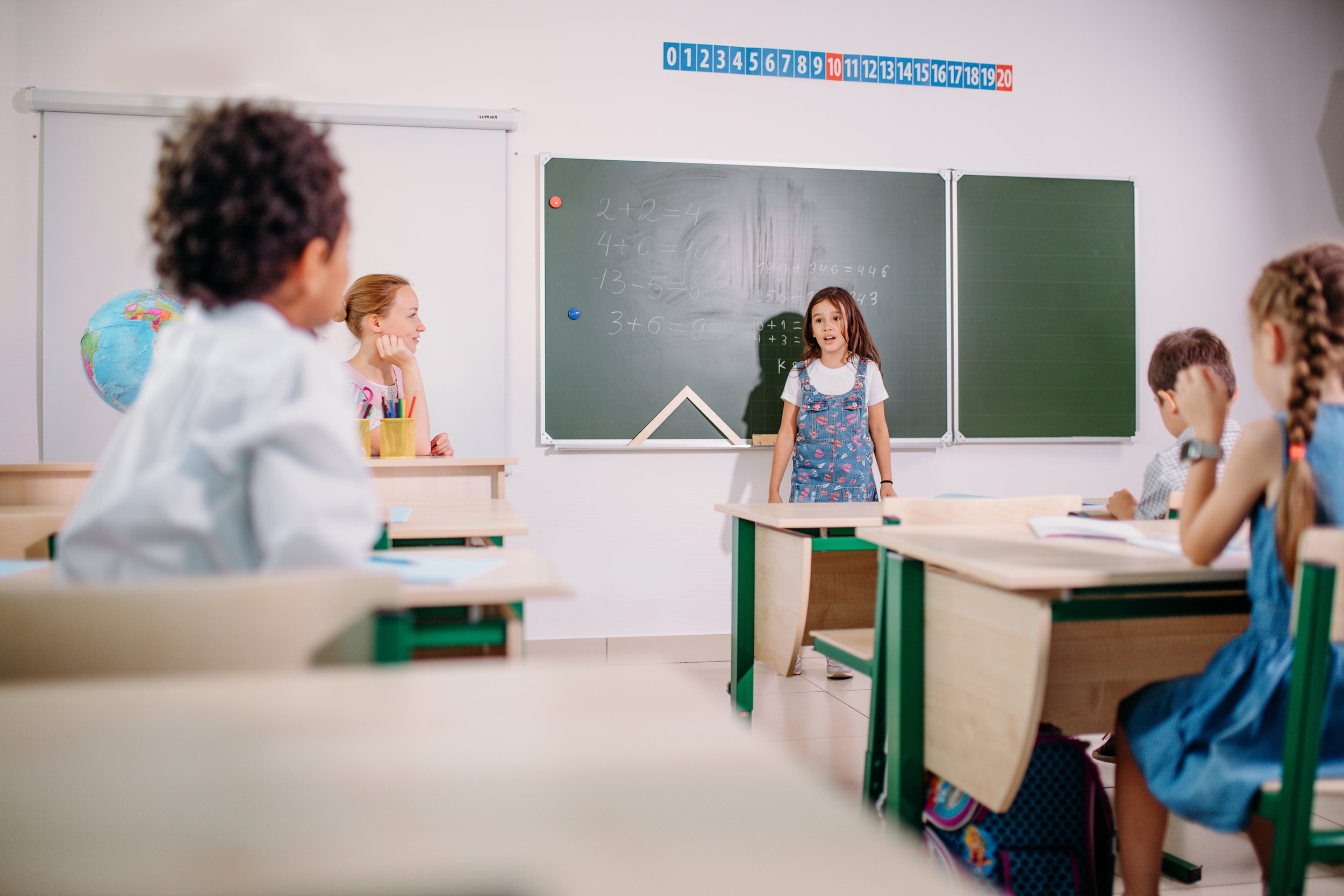 Schülerin präsentiert eine Rechenaufgabe vor der Tafel in einem Klassenzimmer.